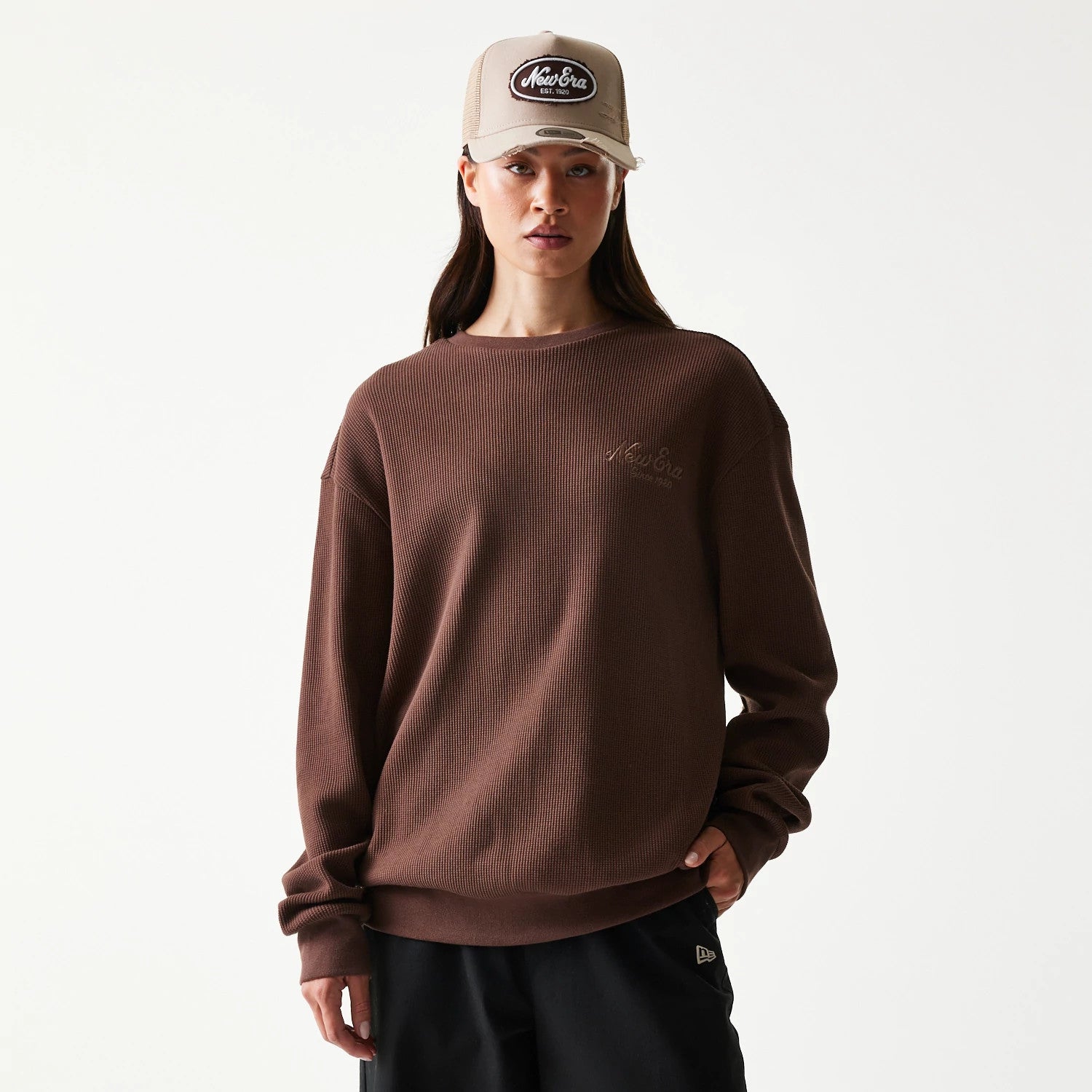 New Era Script Waffle Brown Crew Neck Sweater, front view on a model wearing a beige cap, highlighting the textured waffle knit pattern with New Era script embroidery on the left chest.