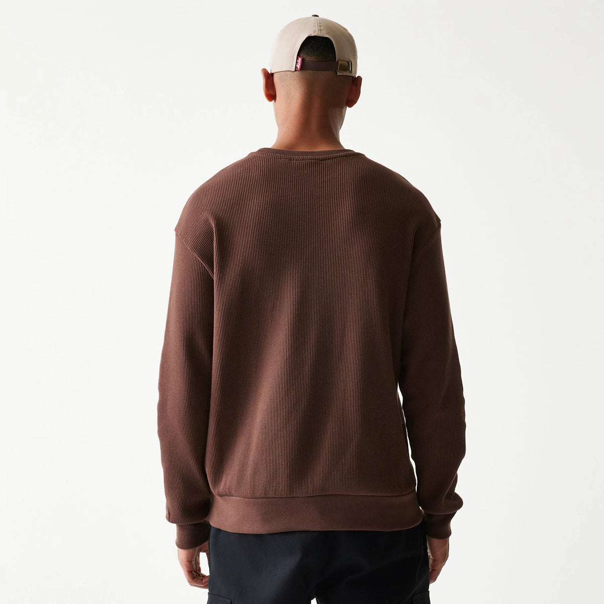 New Era Script Waffle Brown Crew Neck Sweater, back view on a model wearing dark trousers and a light cap, showcasing the ribbed texture and relaxed fit of the brown waffle-knit fabric.