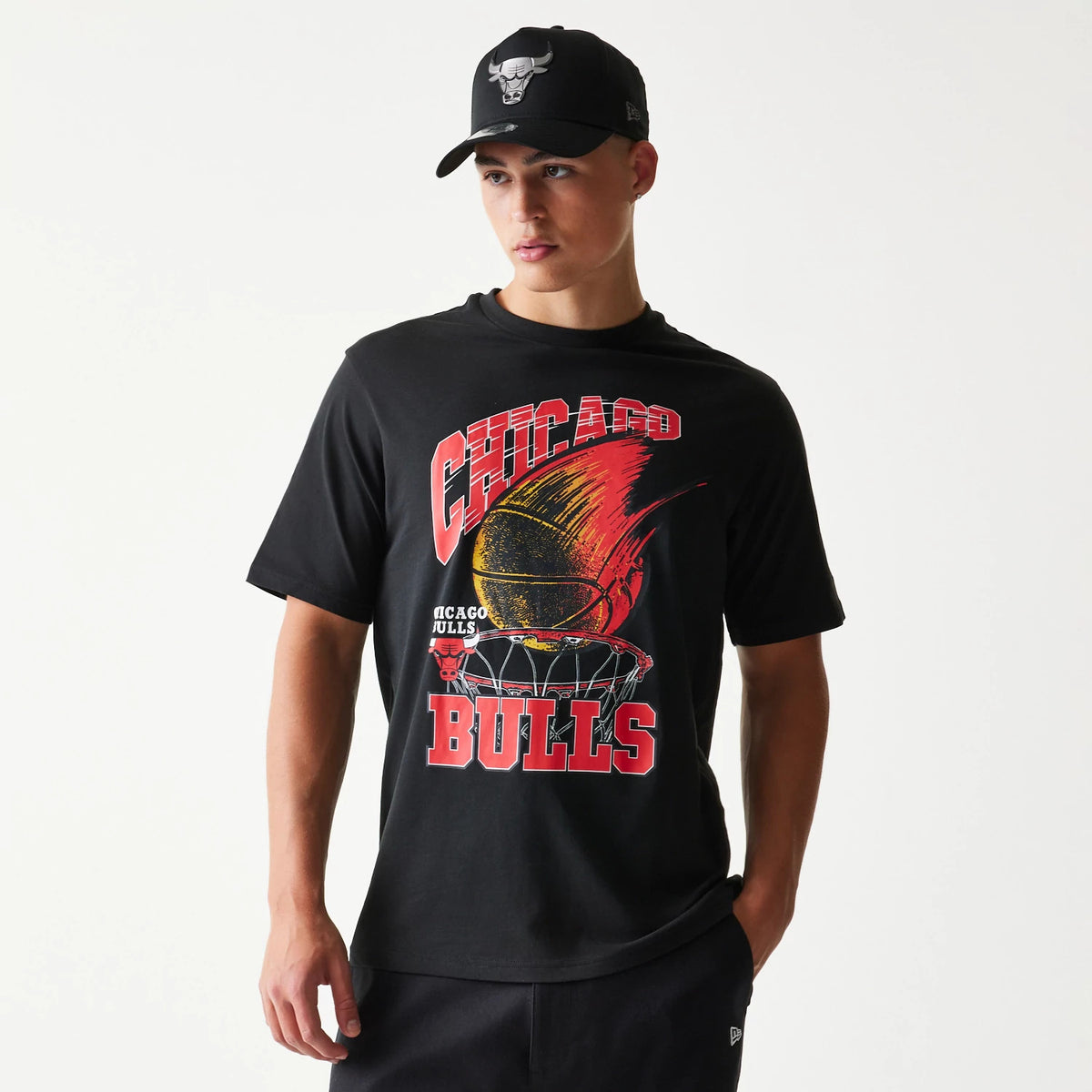 New Era Chicago Bulls NBA Ball Graphic Black T-Shirt, front view on a model with red and orange basketball graphic and CHICAGO BULLS lettering, paired with a black cap featuring an embroidered Bulls logo.
