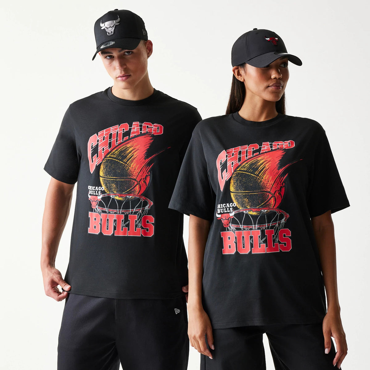 New Era Chicago Bulls NBA Ball Graphic Black T-Shirt, front view on models with matching caps, displaying a graphic of a flaming basketball above a hoop and red Chicago Bulls lettering prominently across the chest.