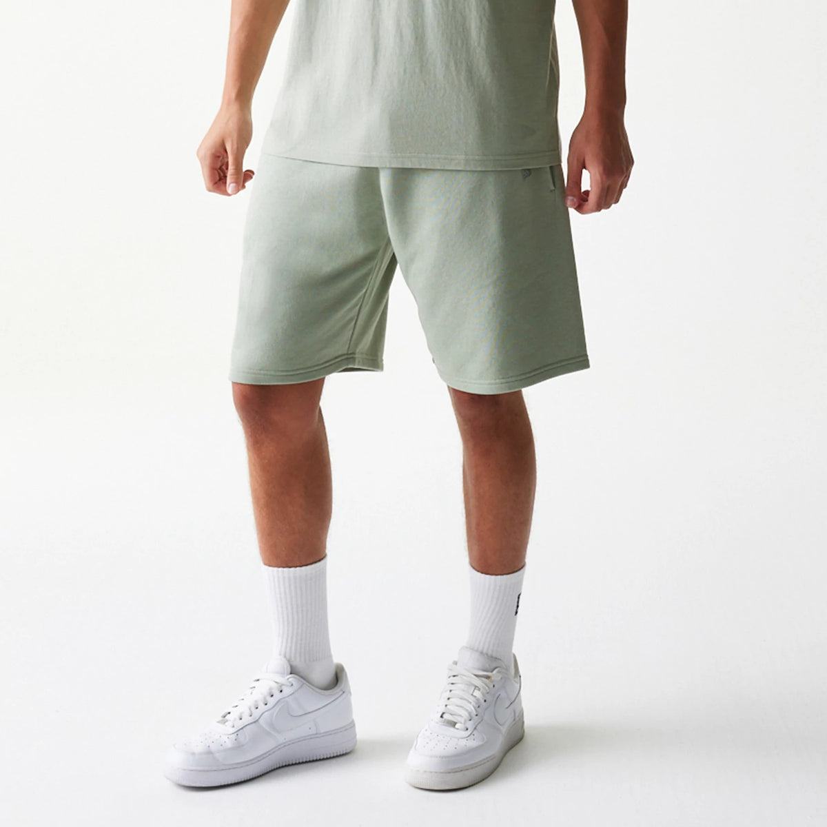 New Era LA Lakers NBA Pastel Green Shorts, front view on a model styled with a matching top, featuring a plain pastel green design, embroidered team logo on the left leg near the hem, and reaching just above the knee.