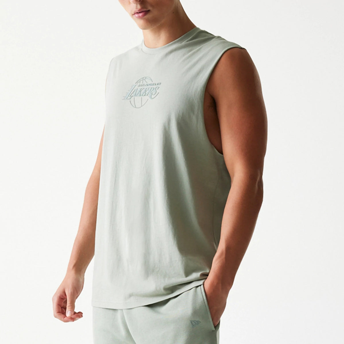 New Era LA Lakers NBA Pastel Green Sleeveless T-Shirt, front view on-model showing a printed team logo in faded green on the chest and a relaxed fit, styled with matching shorts, and a small embroidered New Era logo on the lower left side.
