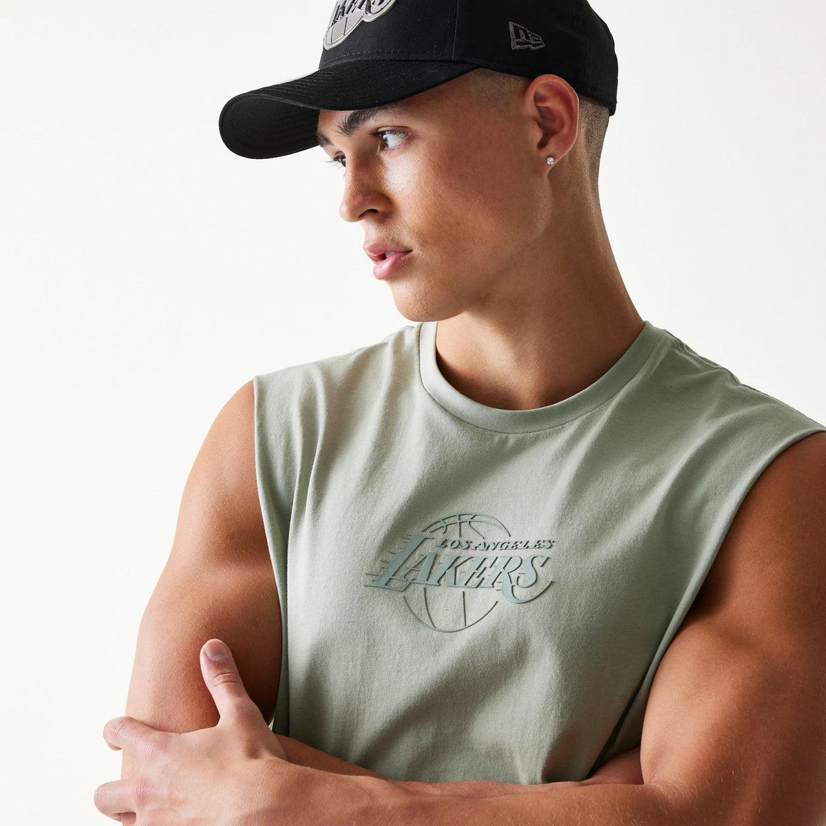New Era LA Lakers NBA Pastel Green Sleeveless T-Shirt, front view on-model showing the pastel green colour with a raised Lakers logo centrally placed on the chest, styled with a black cap displaying an embroidered New Era logo on the side.