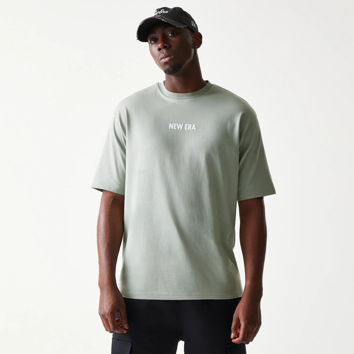 New Era Graphic Pastel Green Oversized T-Shirt, front view on-model featuring the white embroidered New Era logo centred on the chest, with short sleeves and a relaxed fit paired with dark trousers.
