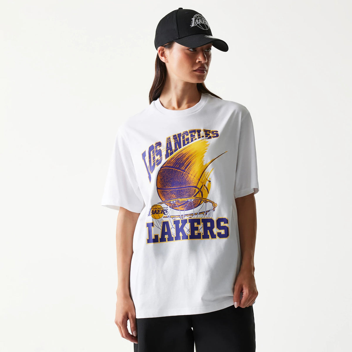 New Era LA Lakers NBA Ball Graphic White T-Shirt, front view on-model showing a dynamic Lakers basketball graphic with Los Angeles Lakers lettering in purple and gold across the chest, paired with a black cap.