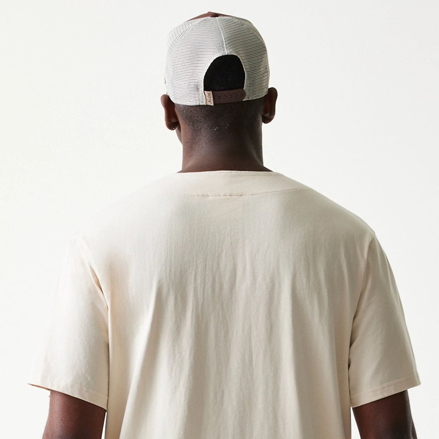 New Era Script Light Beige T-Shirt, back view on a model wearing a mesh cap, showing the plain light beige fabric with short sleeves and a simple round neckline, highlighting the clean and understated design.