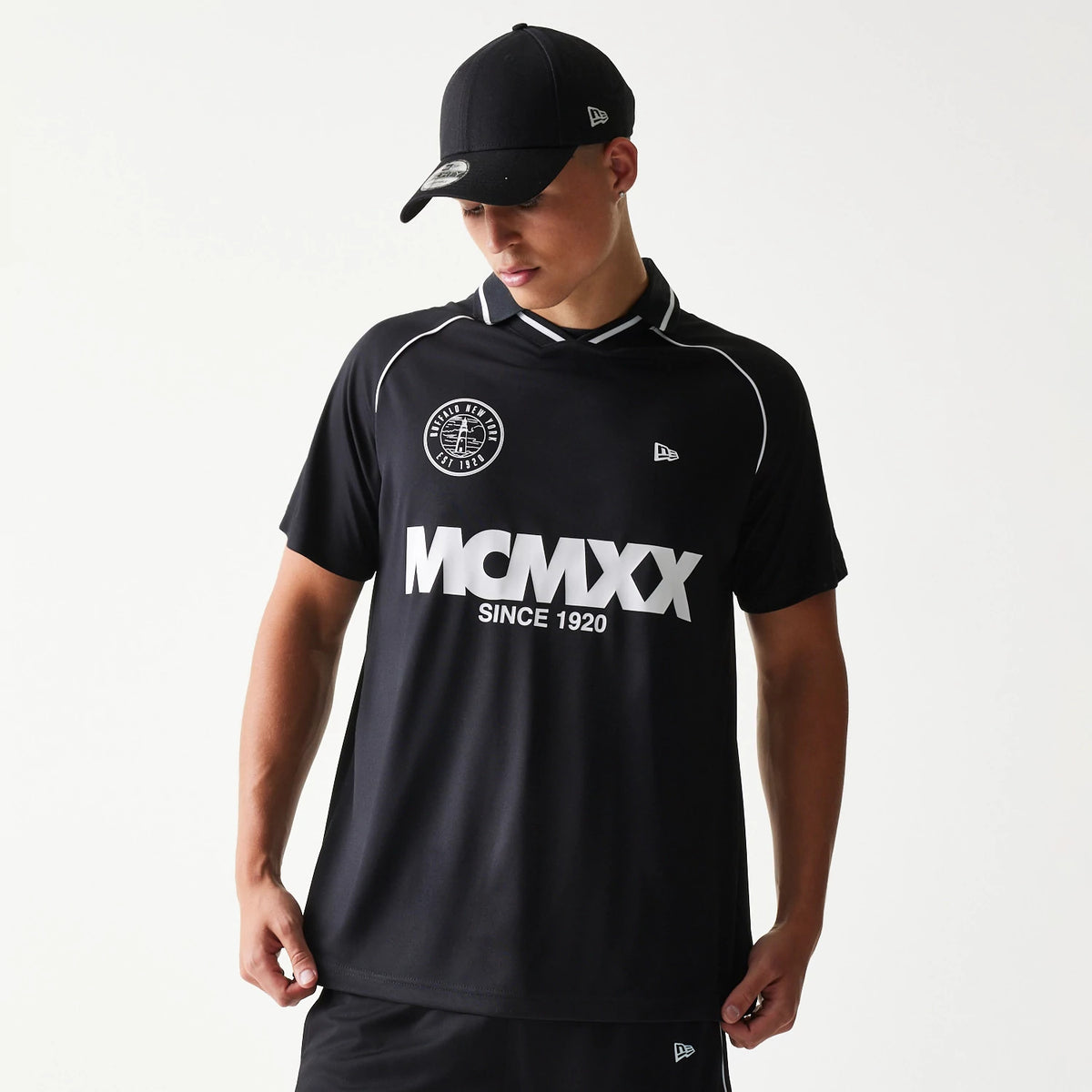 New Era Football Black T-Shirt, front view on-model displaying the large white MCMXX lettering and logo on the chest, an embroidered New Era logo on the left side of the chest, and contrasting white piping along the shoulders.