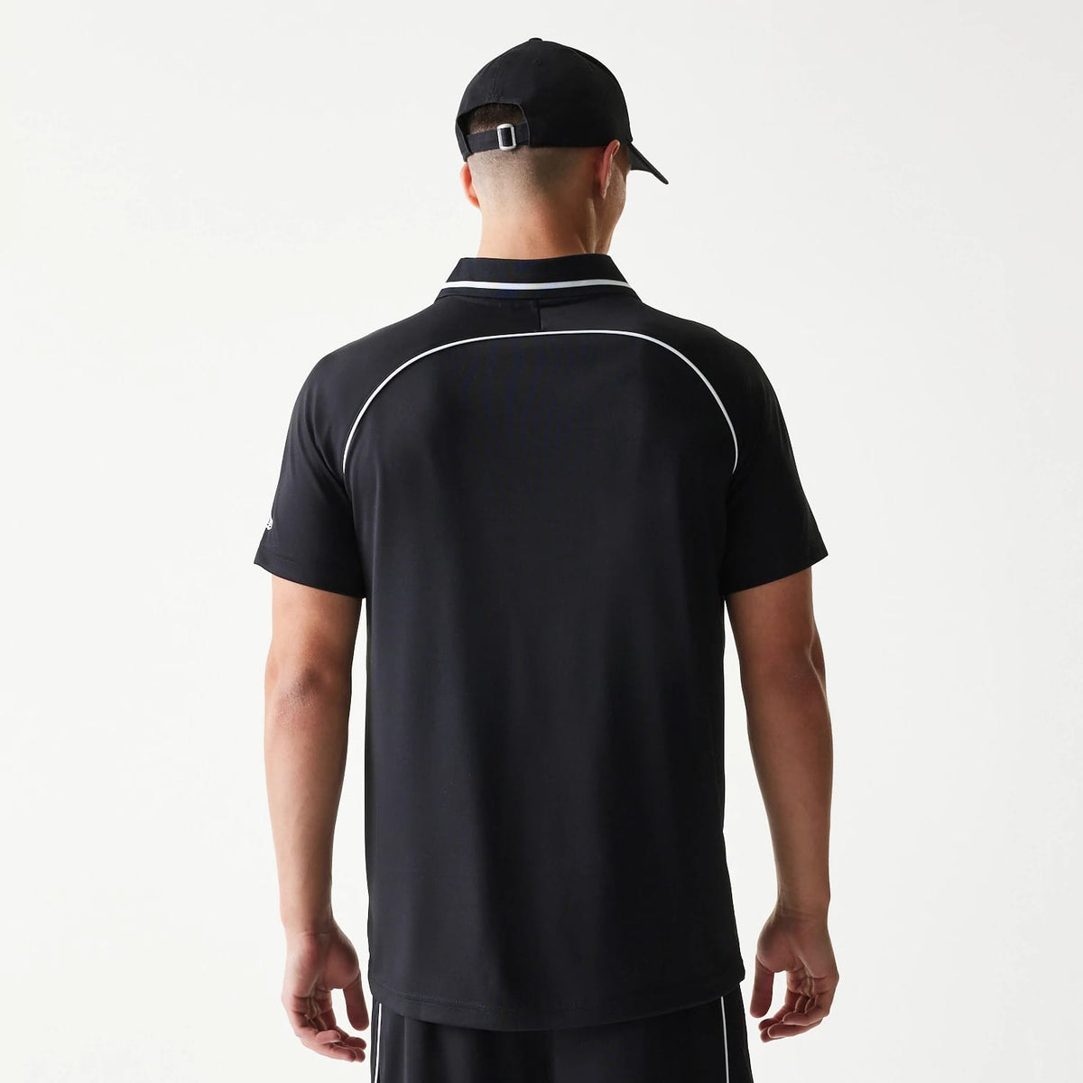 New Era Football Black T-Shirt, back view on a model with a black cap, showing a white piping detail curving across the upper back and the plain black fabric extending down to the straight hem.