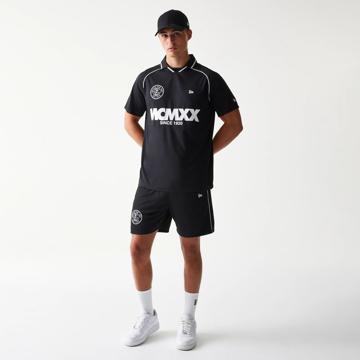 New Era Football Black T-Shirt, front view on-model displaying the white MCMLXX lettering and logo across the chest, a small embroidered New Era logo on the sleeve, and white piping along the collar and sleeves.