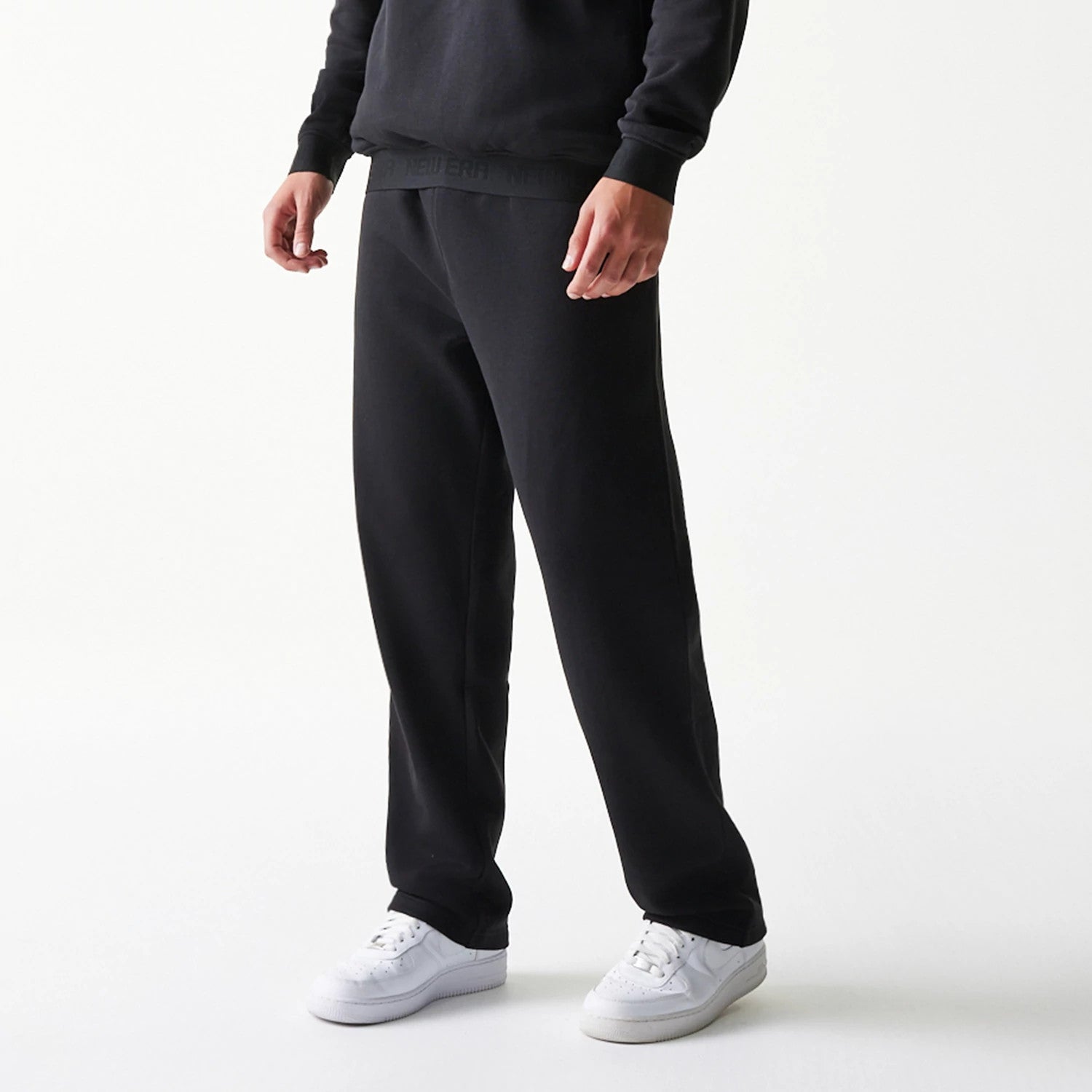 New Era Tech Black on Black Straight Leg Joggers, front view on a model showcasing the relaxed fit and streamlined silhouette, with an elastic waistband featuring the embossed New Era logo, paired with casual white trainers.