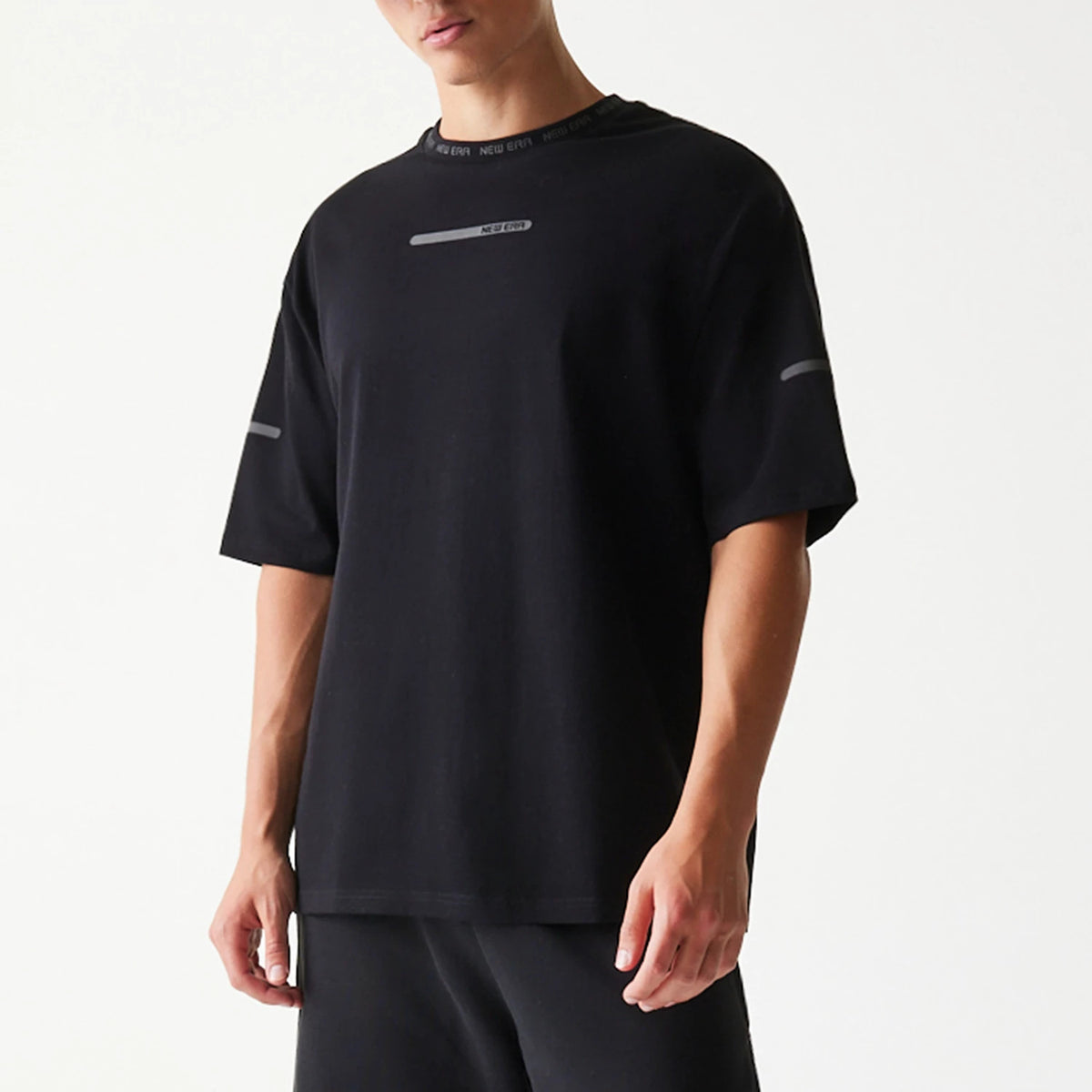 New Era Tech Black Oversized T-Shirt, front view showing a minimalist design with a horizontal stripe and small printed New Era logo on the chest, reflective stripe on the sleeves, and New Era branding on the collar.