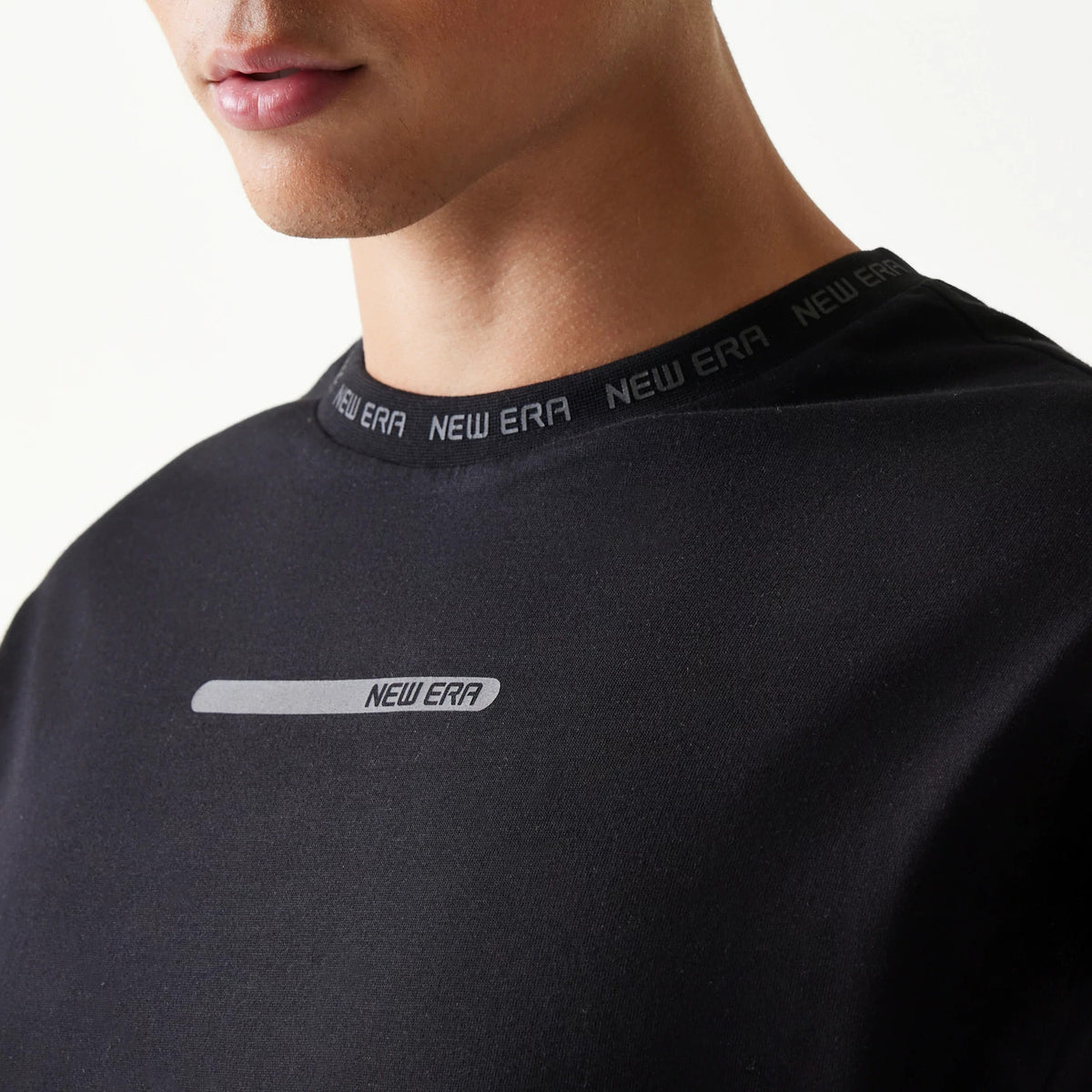 New Era Tech Black Oversized T-Shirt, front view on-model showing a light grey printed New Era logo on the chest and New Era branding along the black neckline, highlighting the and modern design of the garment.