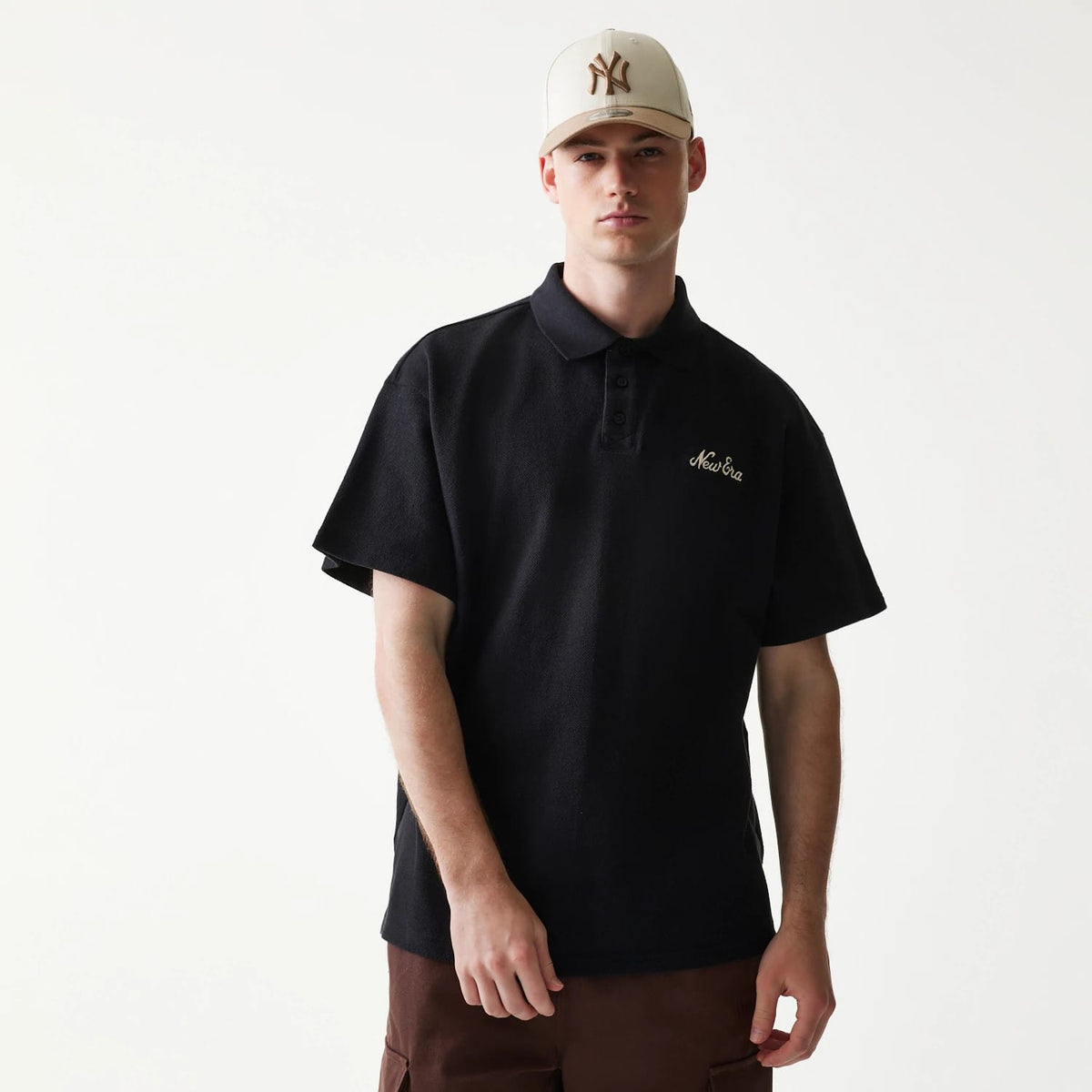 The model is wearing this New Era Graphic Polo T-Shirt in black. 1