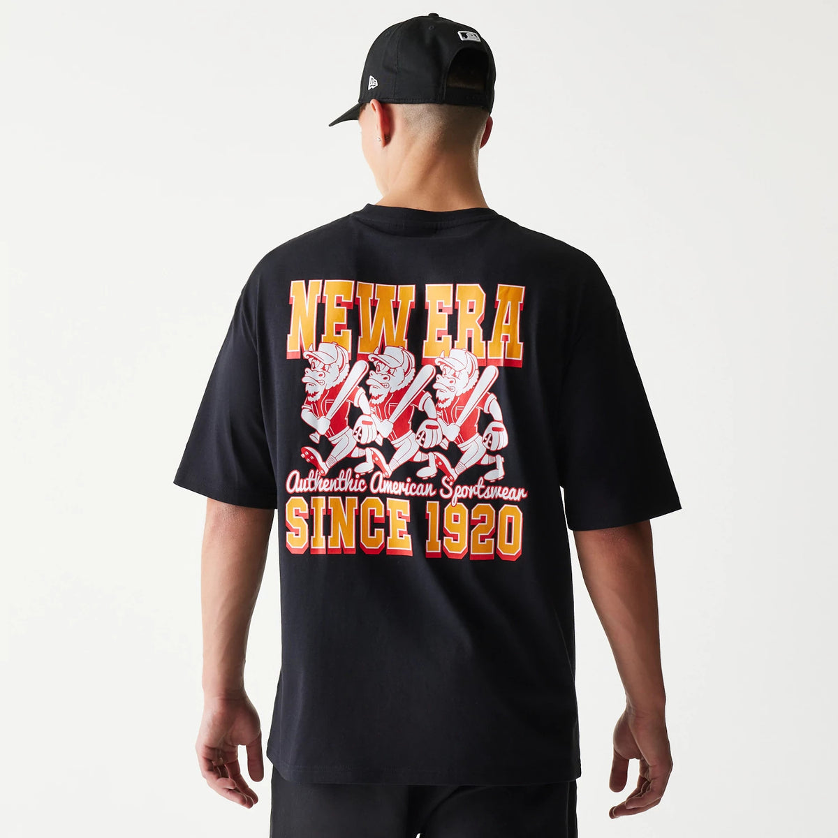 New Era Baseball Cows Character Graphic Black Oversized T-Shirt, back view on a model with a black cap, featuring a retro-style graphic of baseball cows and large New Era lettering with Authentic American Sportswear Since 1920.