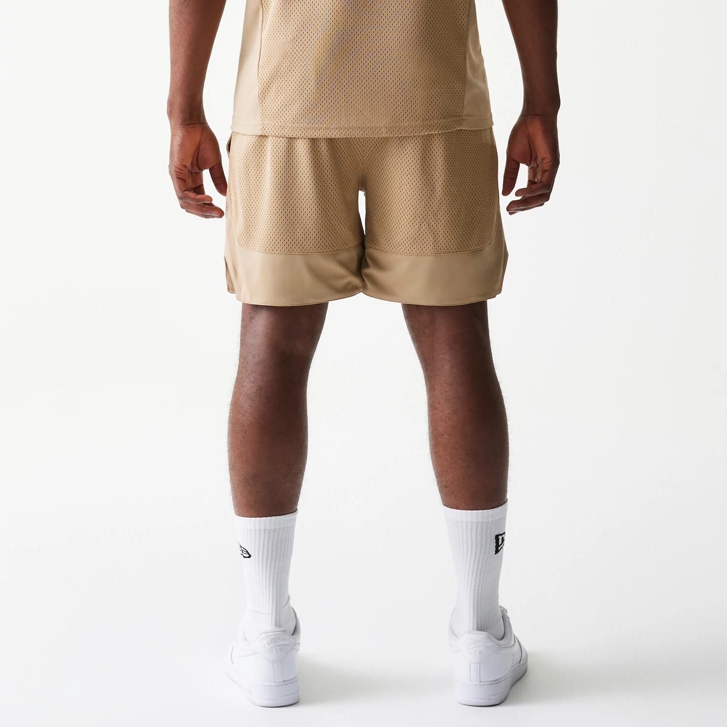New Era Mesh Graphic Light Beige Oversized Shorts, back view on-model displaying the light beige mesh texture across the upper back panel with a lower section, styled with white socks and trainers.