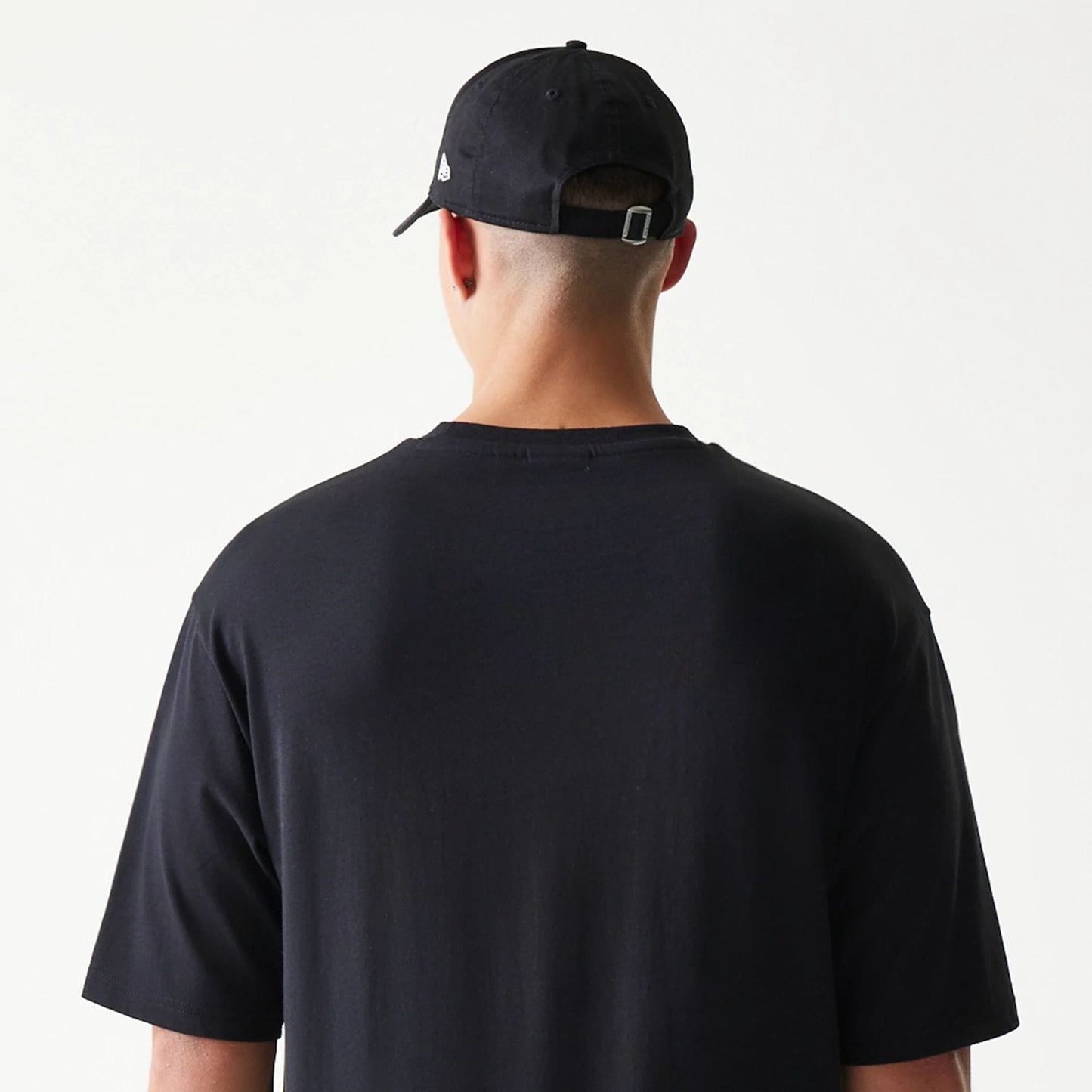 New Era Lemon Fruit Graphic Black Oversized T-Shirt, back view on a model paired with a black cap, showing a clean black design with no graphics, emphasising the loose fit and short sleeves.
