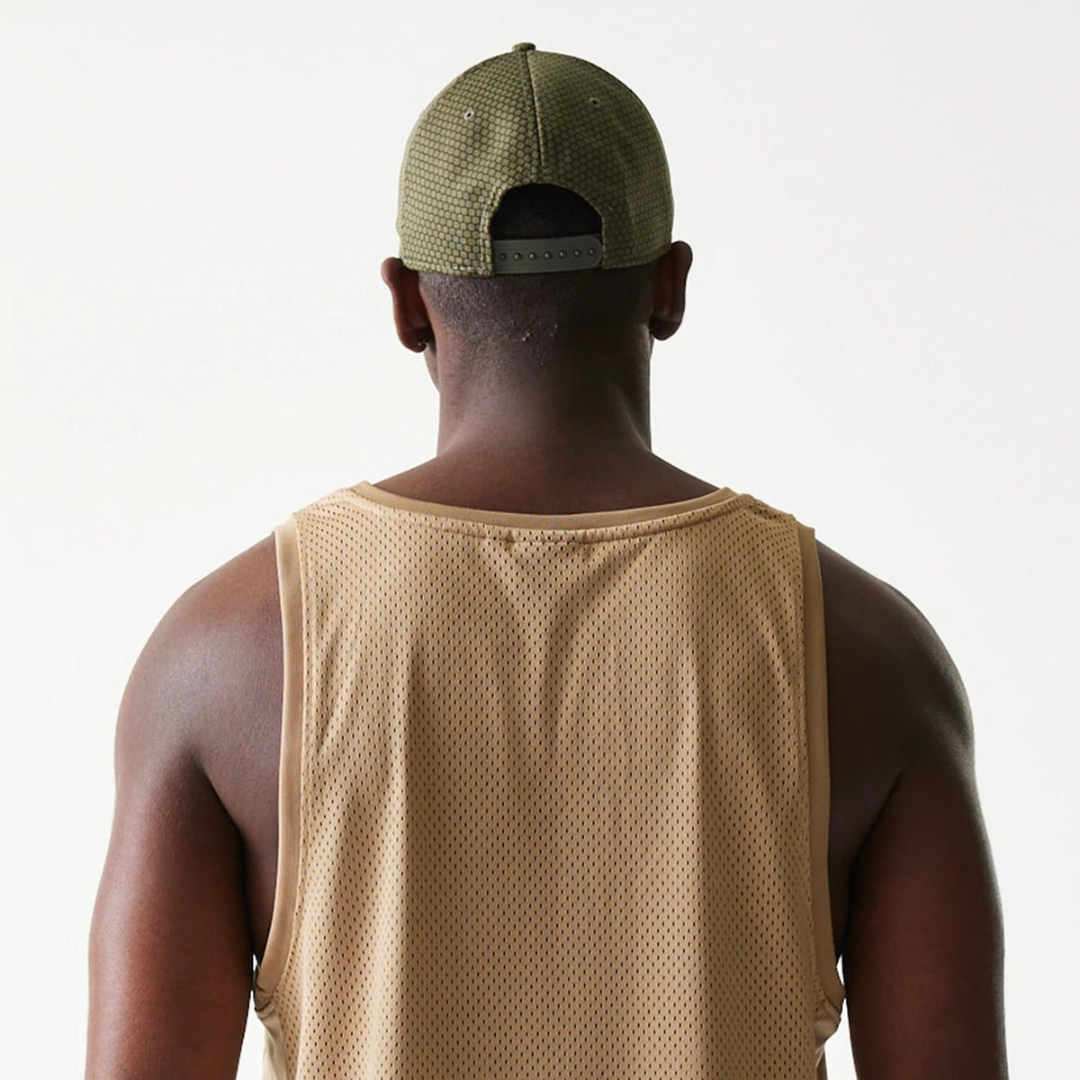 New Era Mesh Light Beige Tank Top, back view on a model highlighting the lightweight mesh fabric structure and light beige colour with wide armholes and a relaxed fit.
