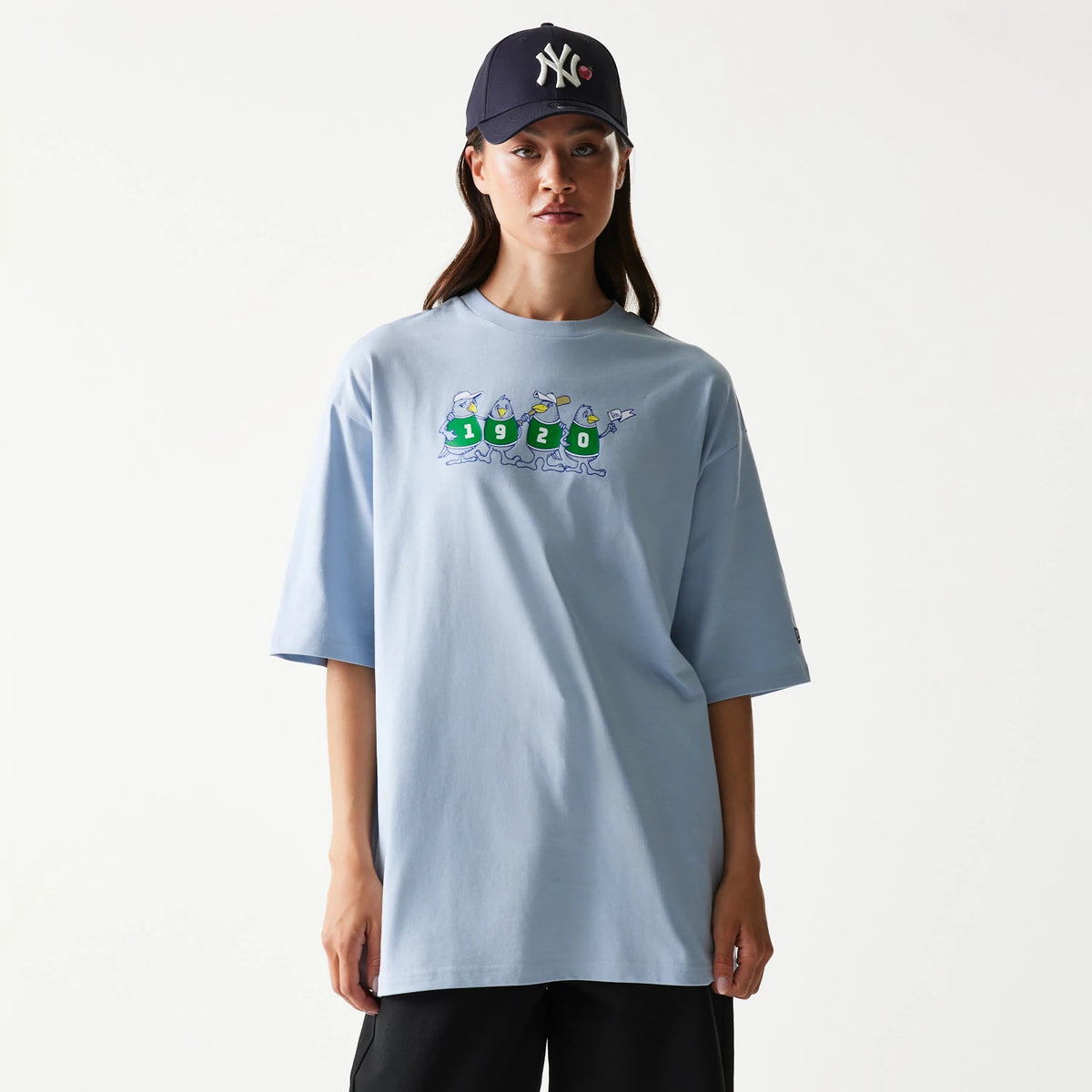 New Era Baseball Birds Character Graphic Blue Oversized T-Shirt, front view on a model wearing a dark cap, featuring a playful graphic of birds in green jerseys with numbers 1920 across the chest.