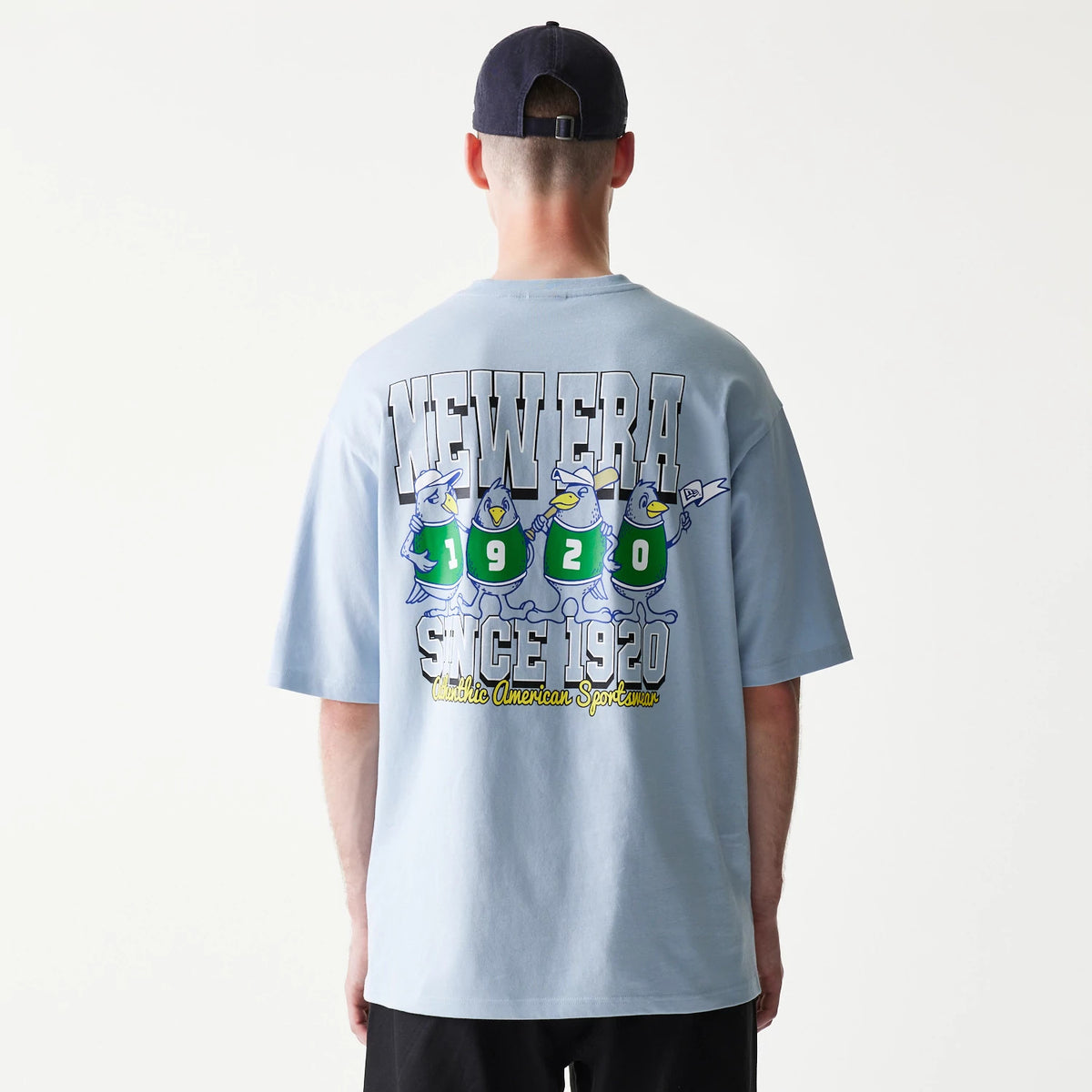 New Era Baseball Birds Character Graphic Blue Oversized T-Shirt, back view on-model displaying cartoon birds in green jerseys numbered 1920, New Era lettering above, and Since 1920 Athletic American Sportswear text below.
