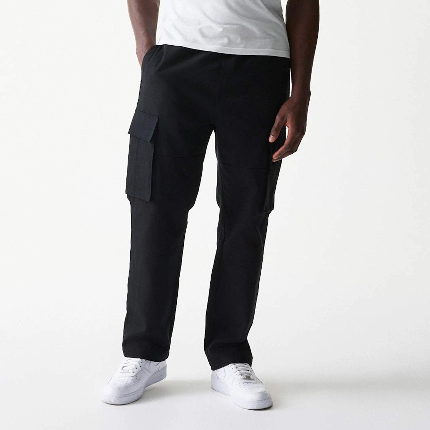 New Era Black Straight Leg Cargo Joggers, front view on a model showing black cargo pockets on each thigh, straight leg design, and elasticated waistband, paired with white trainers for a casual look.