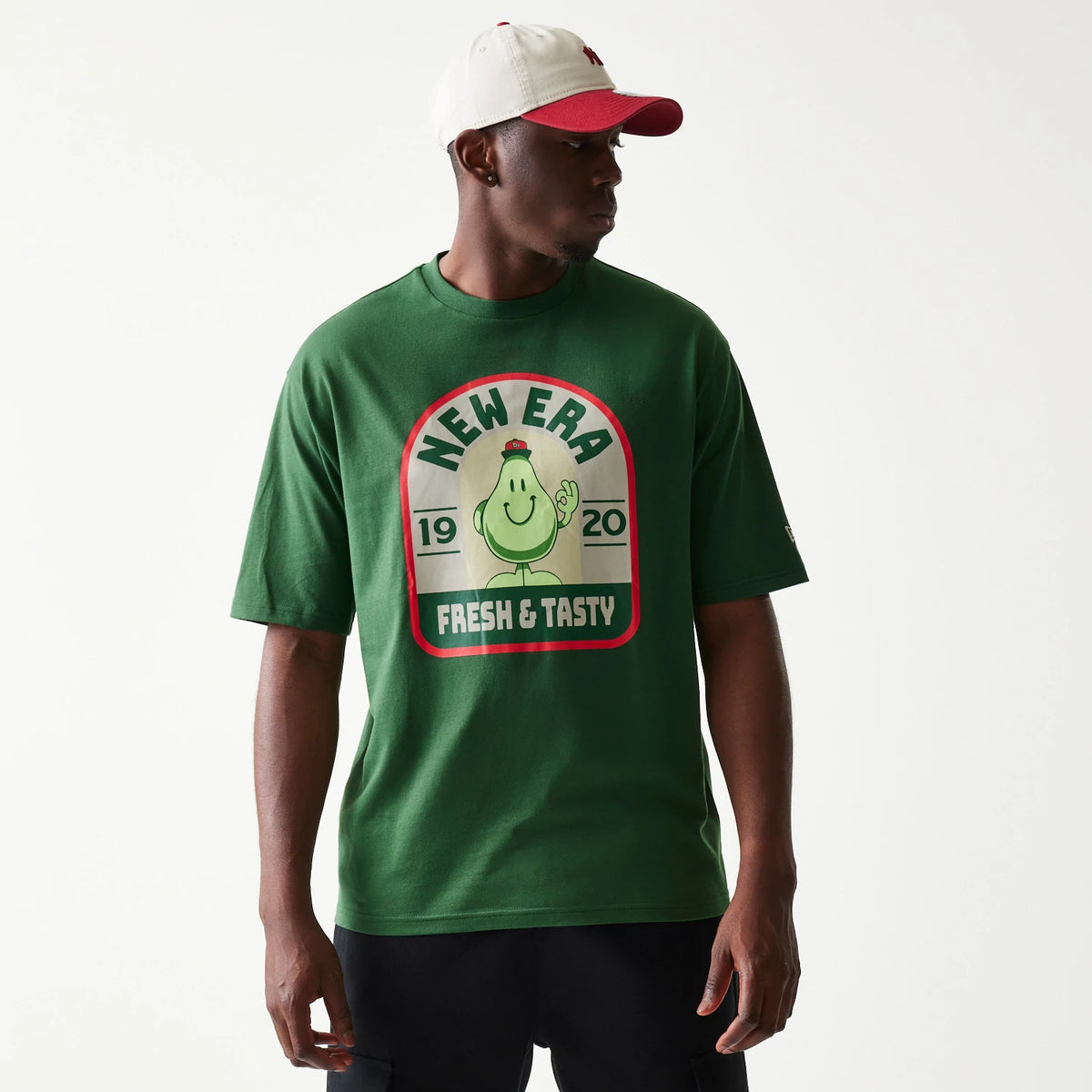New Era Pear Fruit Graphic Dark Green Oversized T-Shirt, front view on-model featuring a large central graphic of a cartoon pear with Fresh & Tasty text, New Era logo printed at the centre chest, styled with black shorts and a contrasting white.