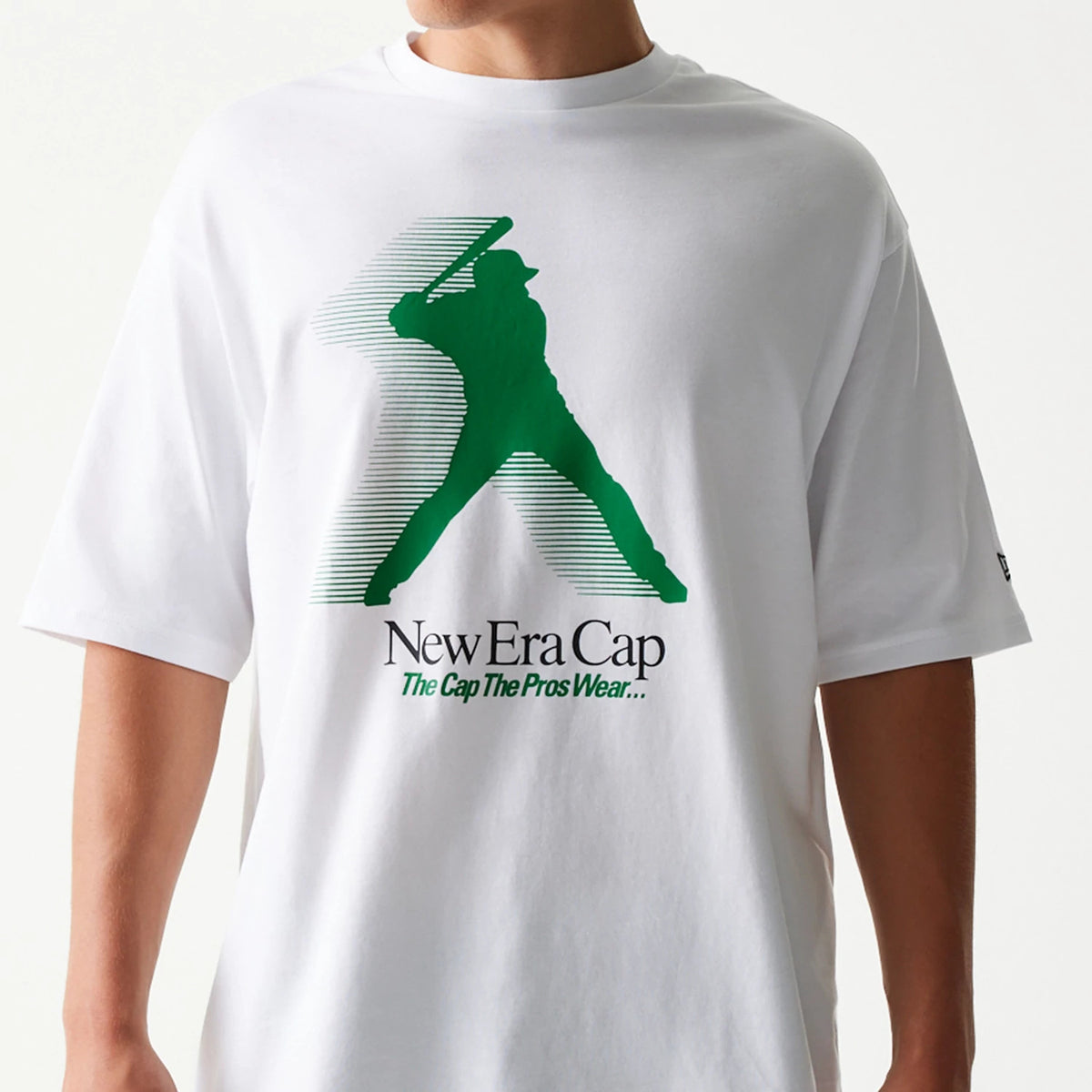 New Era Baseball Player Graphic White Oversized T-Shirt, front view showing a large green silhouette of a baseball player with a bat across the chest, black printed New Era Cap lettering below, and styled on-model for a loose fit.