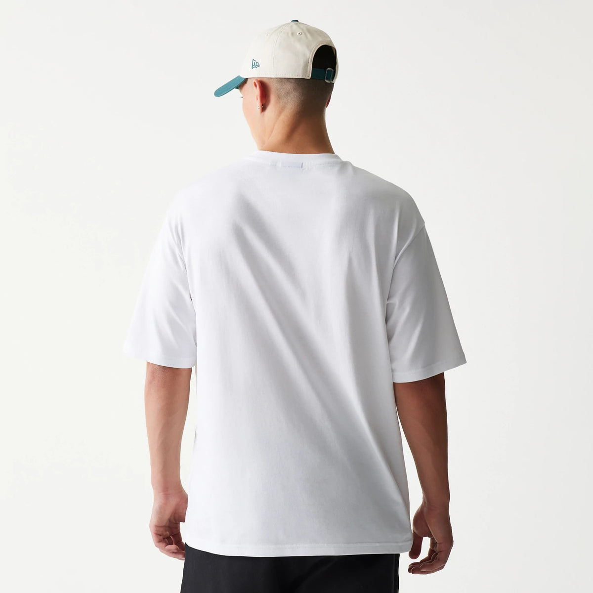 New Era Baseball Player Graphic White Oversized T-Shirt, back view on a model wearing a contrasting cap, showing the plain white fabric with a relaxed fit and short sleeves hanging loosely from the shoulders.