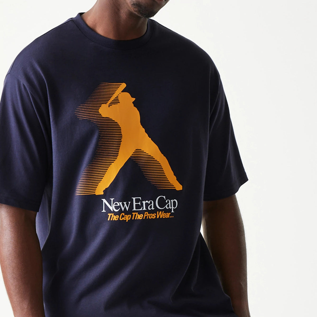 New Era Baseball Player Graphic Navy Oversized T-Shirt, front view showing an orange graphic of a baseball player swinging a bat across the chest with the New Era Cap logo and tagline in white and orange below.