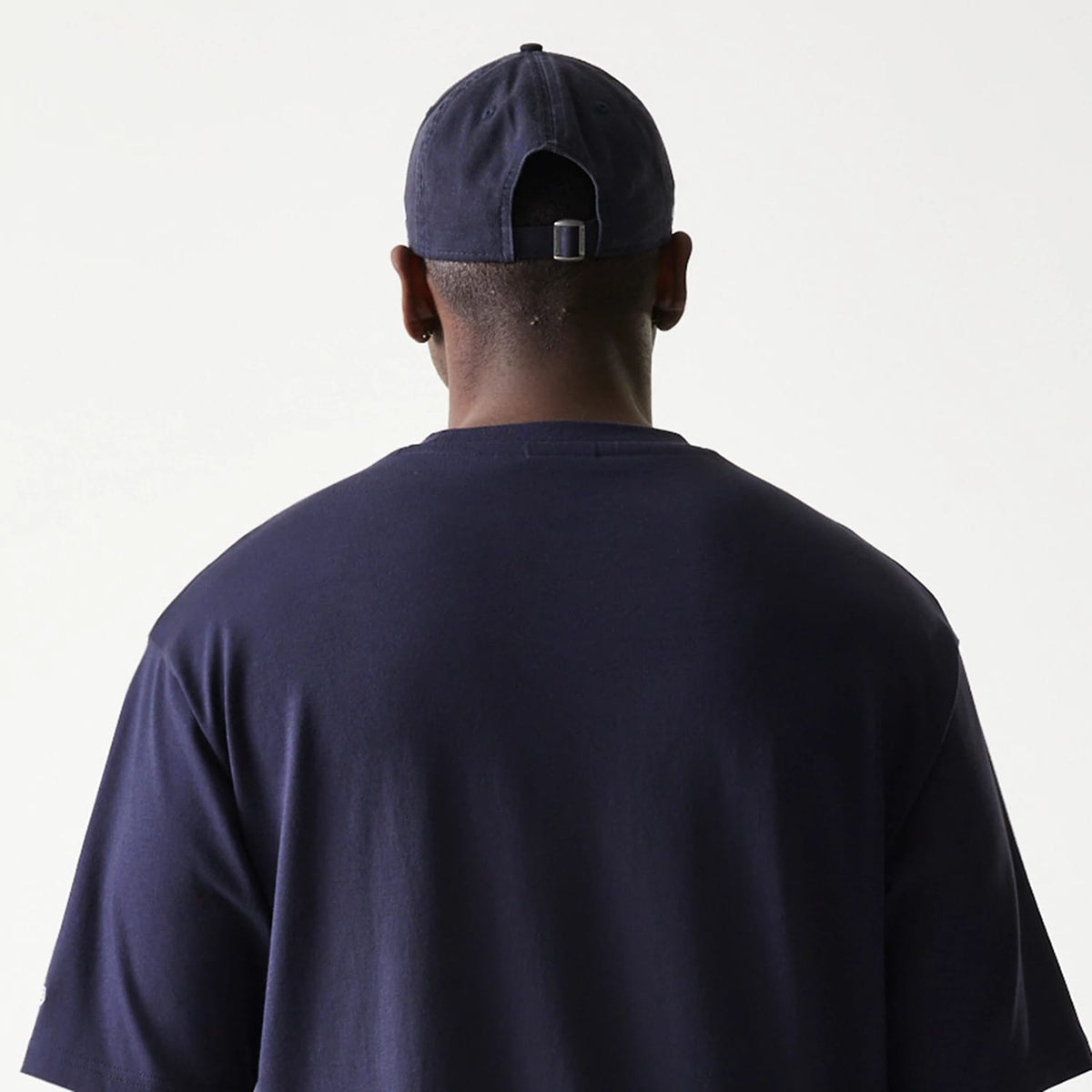 New Era Baseball Player Graphic Navy Oversized T-Shirt, back view on a model wearing a plain navy cap, showing the simple navy design without any graphics or logos on the oversized back.