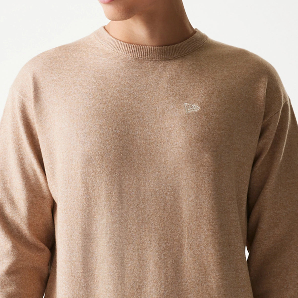 New Era Essential Flag Light Beige Knitted Sweater, front view on a model showing the embroidered white New Era flag logo on the left chest and a ribbed crew neck, highlighting the soft, light beige knit fabric.