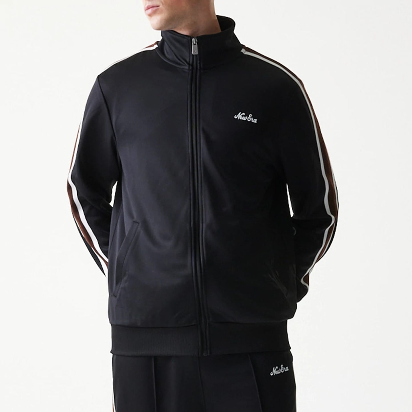 New Era Script Black Track Jacket, front view on-model showing the black jacket with a white embroidered New Era logo on the left chest, full zip closure, and white side stripes running down the length of the sleeves.