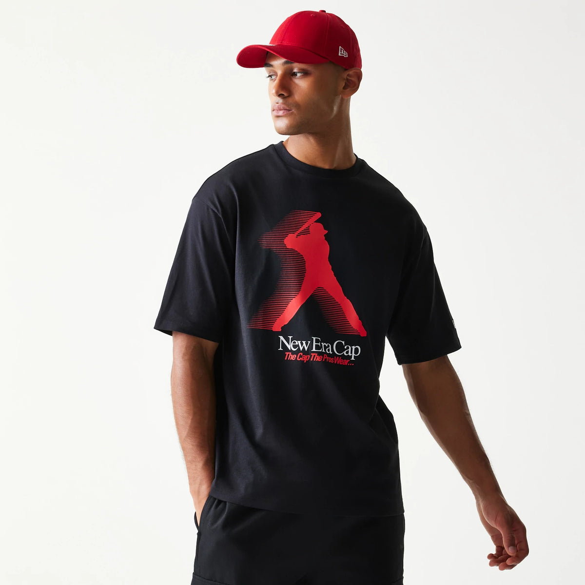 New Era Baseball Player Graphic Black Oversized T-Shirt, front view on a model featuring a large red graphic of a baseball player mid-swing, with New Era Cap The Cap The Pros Wear printed below the design.