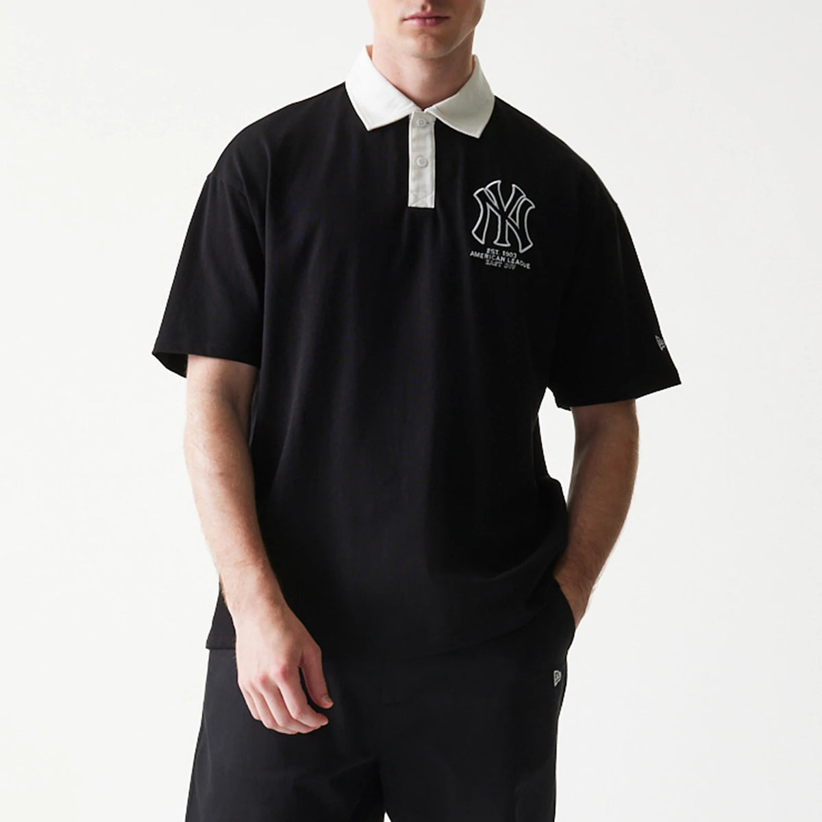 New Era New York Yankees MLB Black Oversized Polo T-Shirt, front view on a model wearing matching black trousers, featuring a large embroidered Yankees logo on the left chest and a white collar contrasting with the black fabric.