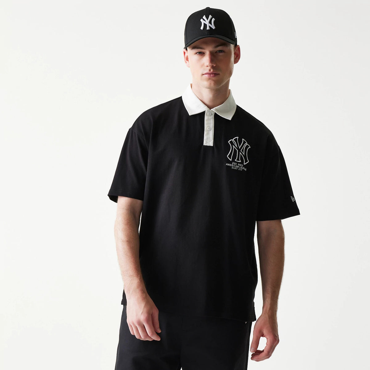 New Era New York Yankees MLB Black Oversized Polo T-Shirt, front view on-model showing an embroidered Yankees logo on the left chest with contrasting white collar and placket, and a New Era logo embroidered on the left sleeve.