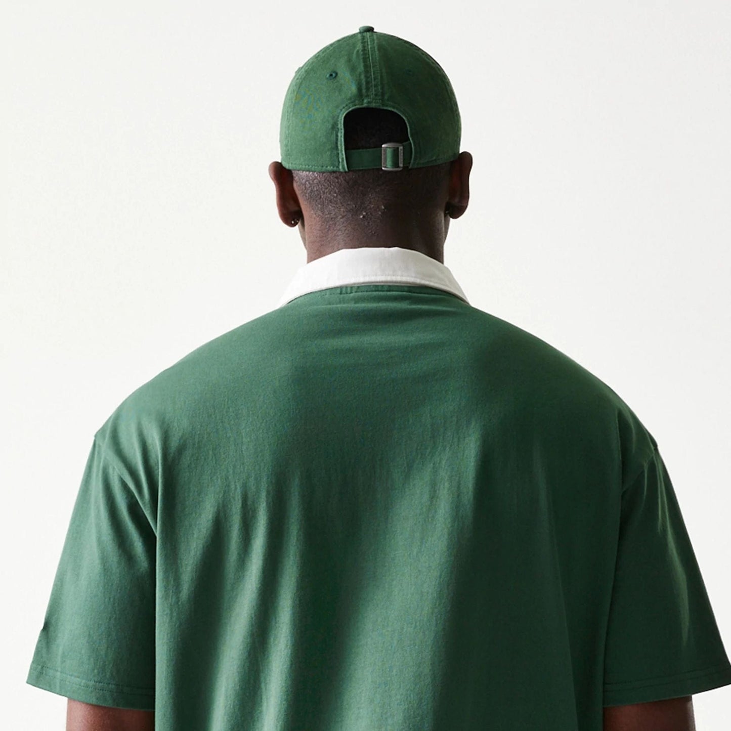 New Era LA Dodgers MLB Dark Green Oversized Polo T-Shirt, back view on a model with a dark green cap, featuring a white collar contrasting with the dark green fabric, and short sleeves extending to the elbows.