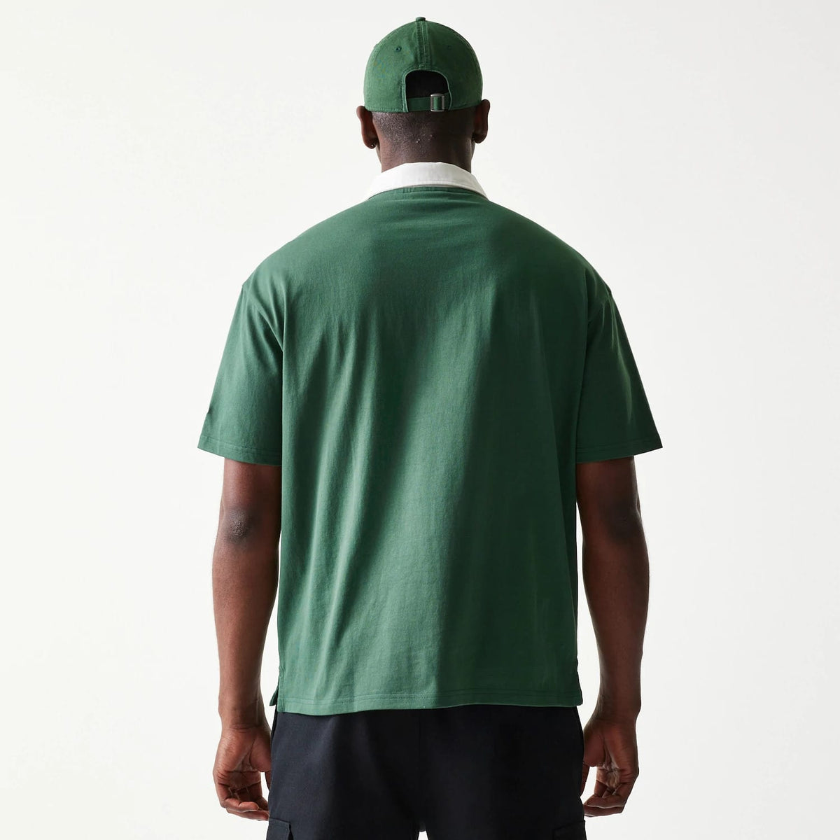 New Era LA Dodgers MLB Dark Green Oversized Polo T-Shirt, back view on-model showcasing the plain dark green back with short sleeves, under a white collar, paired with a matching dark green cap displaying eyelets and an adjustable strap at the back.