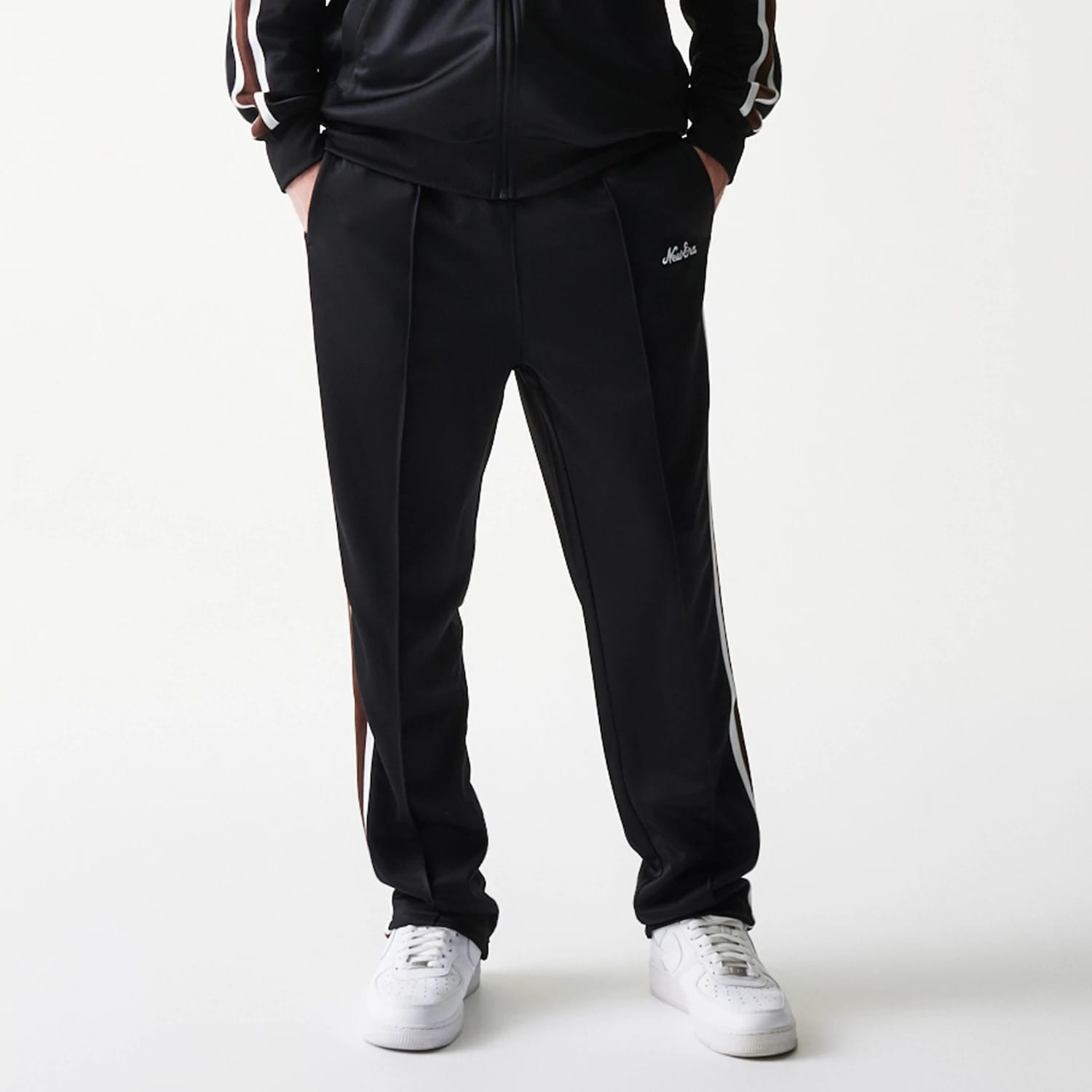 New Era Script Black Straight Leg Joggers, front view showing the white New Era script logo on the left pocket area, with side strip and a relaxed fit around the ankles paired with white trainers.