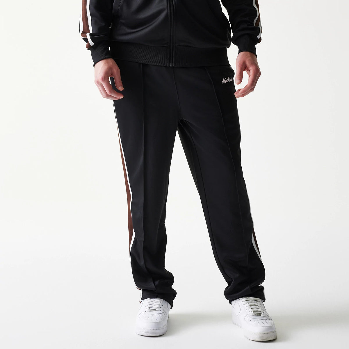 New Era Script Black Straight Leg Joggers, front view on a model with white trainers, showing the embroidered New Era script logo on the left hip and contrasting side stripes on the black material.