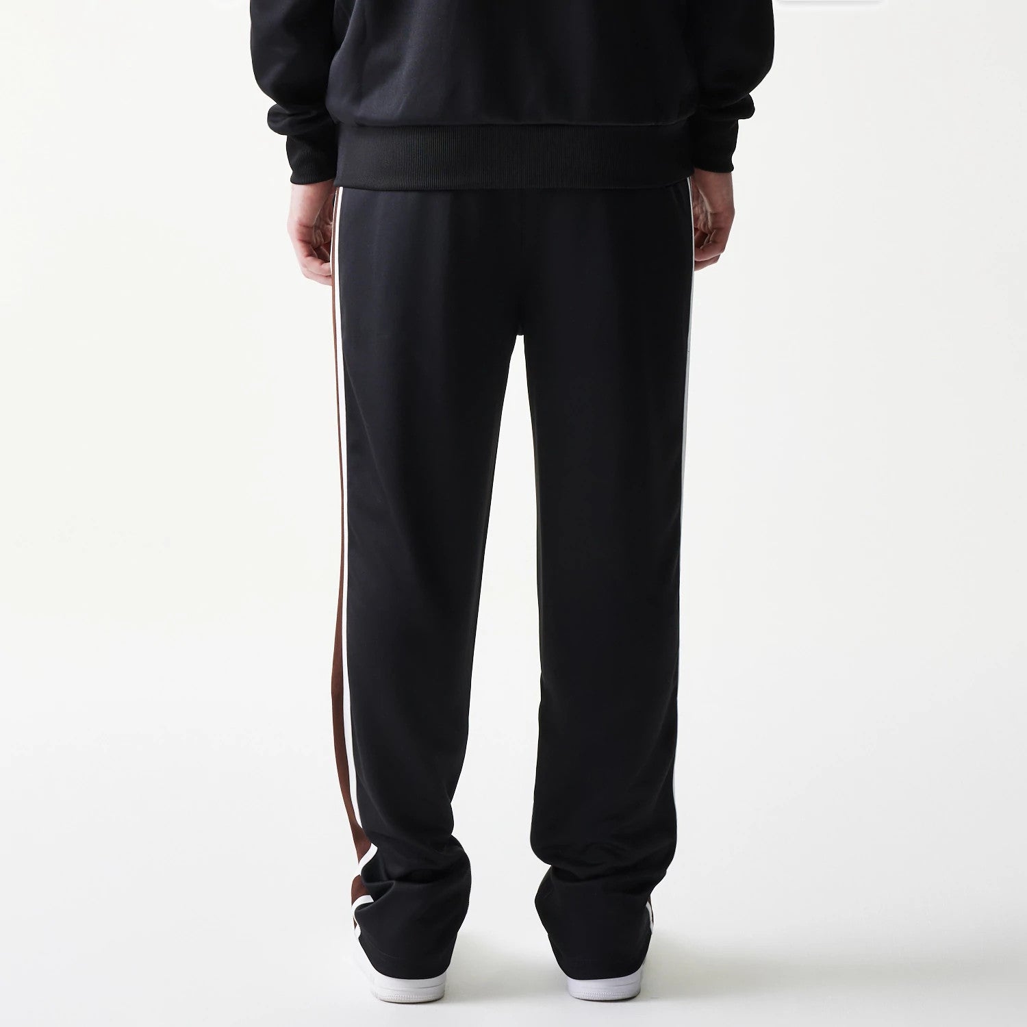 New Era Script Black Straight Leg Joggers, rear view on a model showing the full-length black joggers with white and brown side stripes, elasticated waistband, and relaxed fit over white trainers.