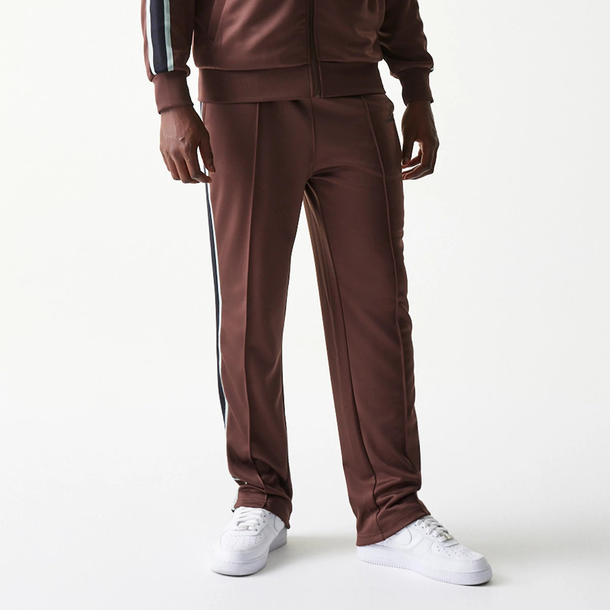 New Era Script Brown Straight Leg Joggers, front view on a model showing the brown fabric with a finish, featuring a black and white side stripe along the legs, complemented by white trainers.