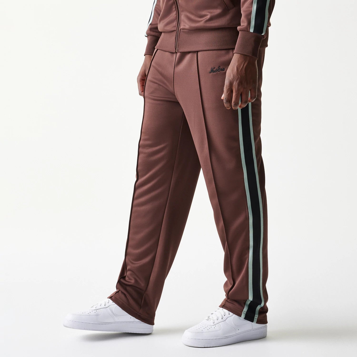 New Era Script Brown Straight Leg Joggers, front view on a model showing the black embroidered New Era script logo on the upper left leg, with black and mint green stripes running down the sides.