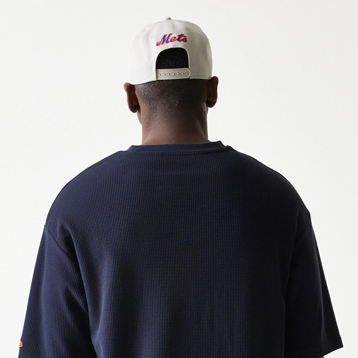New Era New York Mets MLB Waffle Navy Oversized T-Shirt, back view on-model showing the textured navy fabric, with the person wearing a white cap featuring an embroidered Mets logo in red and blue on the back.