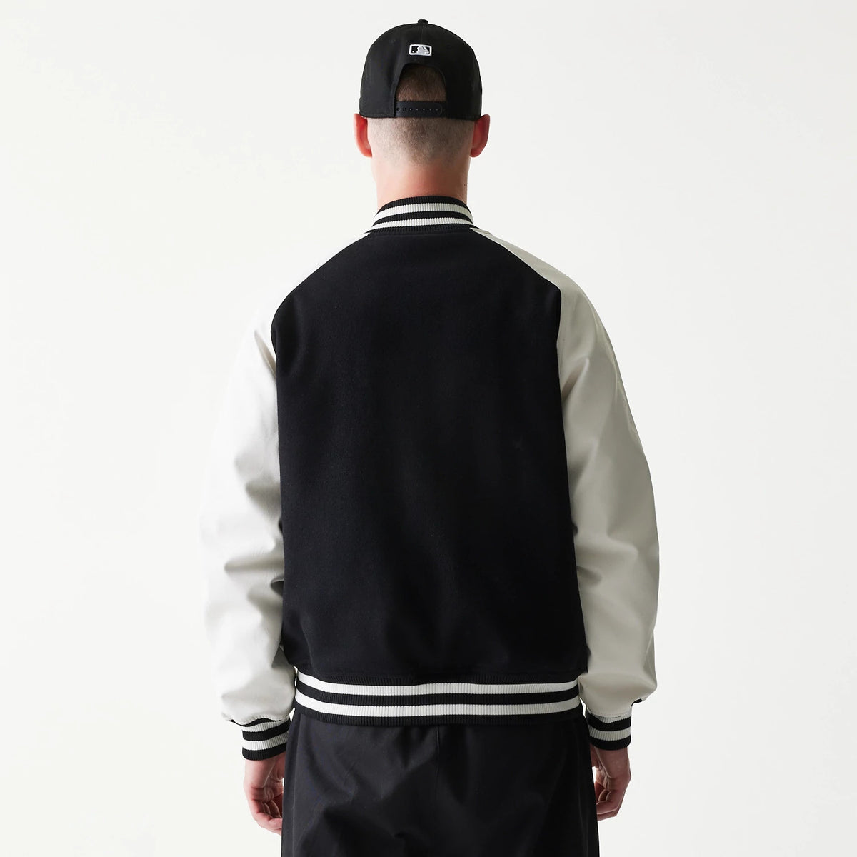 New Era New York Yankees MLB Black Varsity Jacket, back view on-model showing the solid black back panel, contrasting white sleeves and a black and white striped ribbed collar, cuffs, and hem.