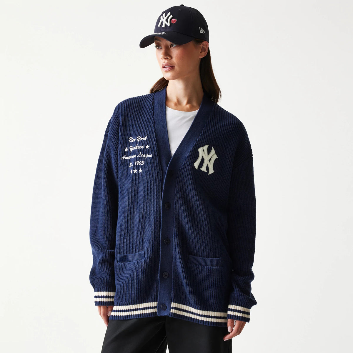 New Era New York Yankees MLB Collegiate Navy Cardigan, front view on a model showing the white embroidered NY logo on the left chest and lettering on the right, with striped cuffs and hem, paired with a matching navy cap.