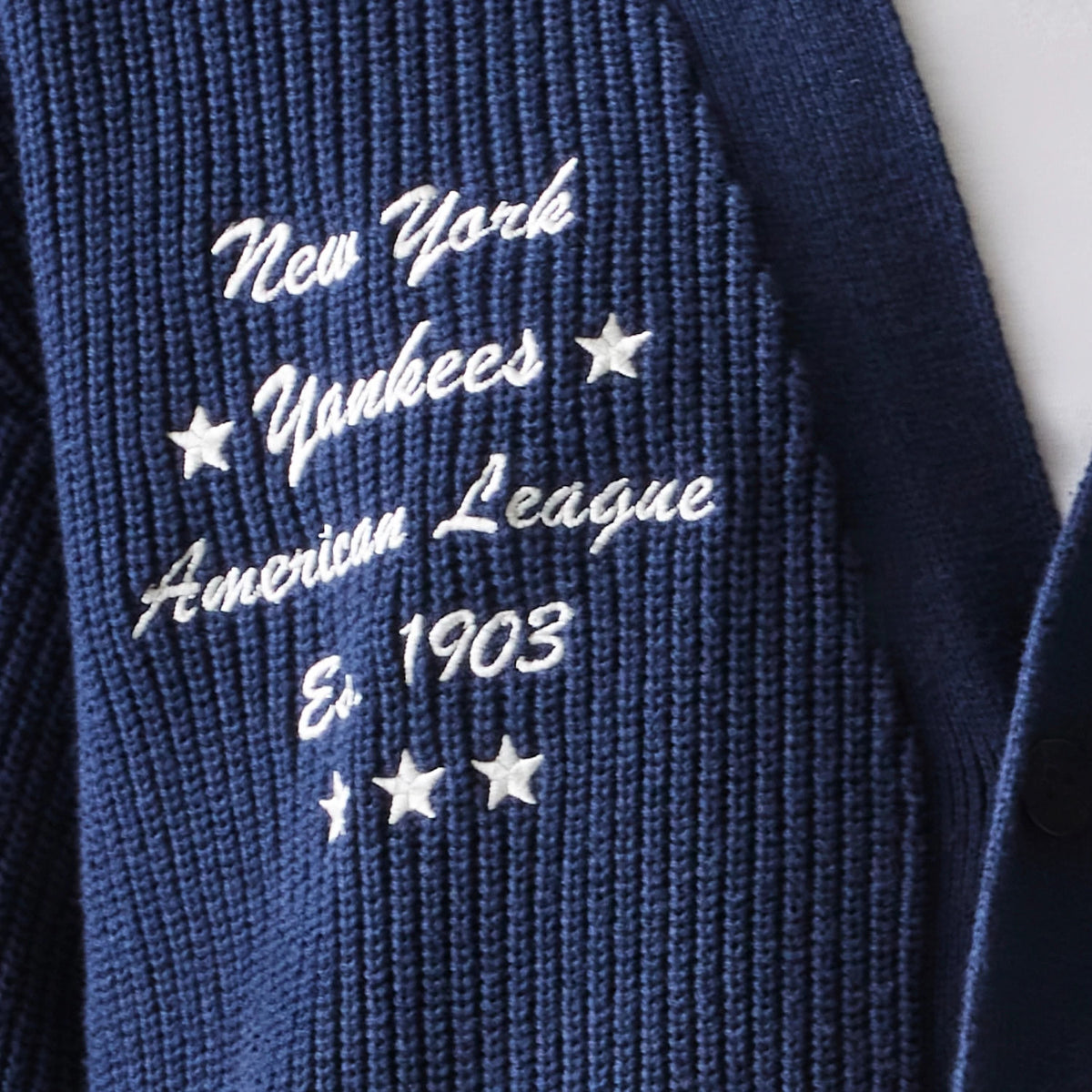 New Era New York Yankees MLB Collegiate Navy Cardigan, close-up view showing white embroidered text and stars with phrases New York Yankees, American League, and Est. 1903 on the textured navy knit fabric.