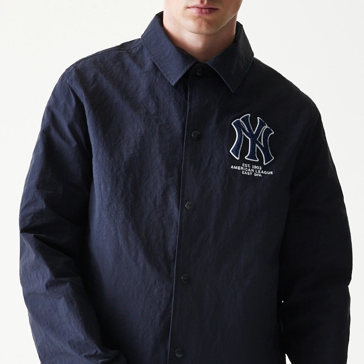 New Era New York Yankees MLB Coaches Navy Jacket, front view on-model showing the embroidered NY logo on the left chest with additional lettering beneath, black button closure down the centre, and a classic pointed collar.