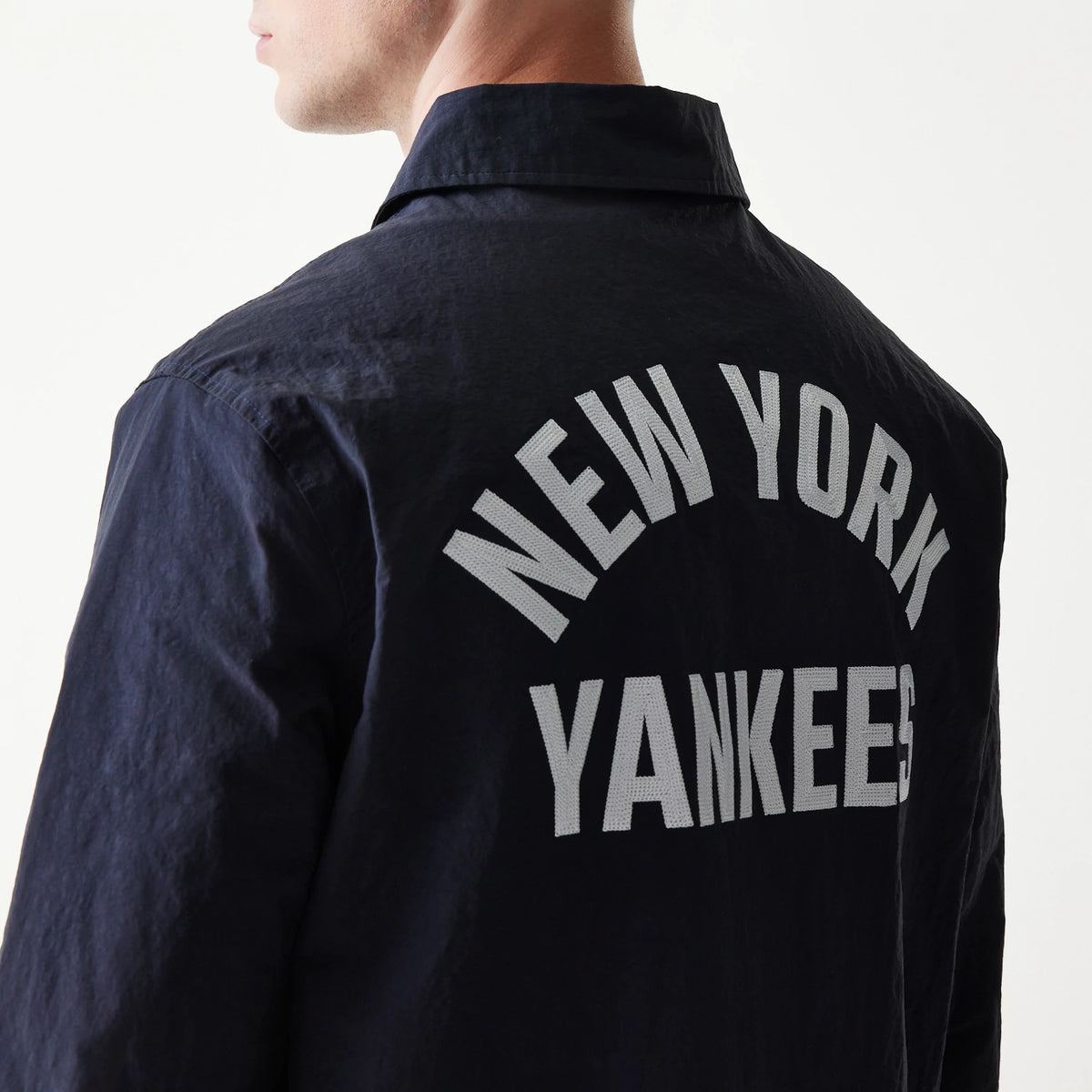 New Era New York Yankees MLB Coaches Navy Jacket, three-quarter view showing the large white embroidered New York Yankees lettering arching across the upper back, worn by a model with the collar slightly raised.