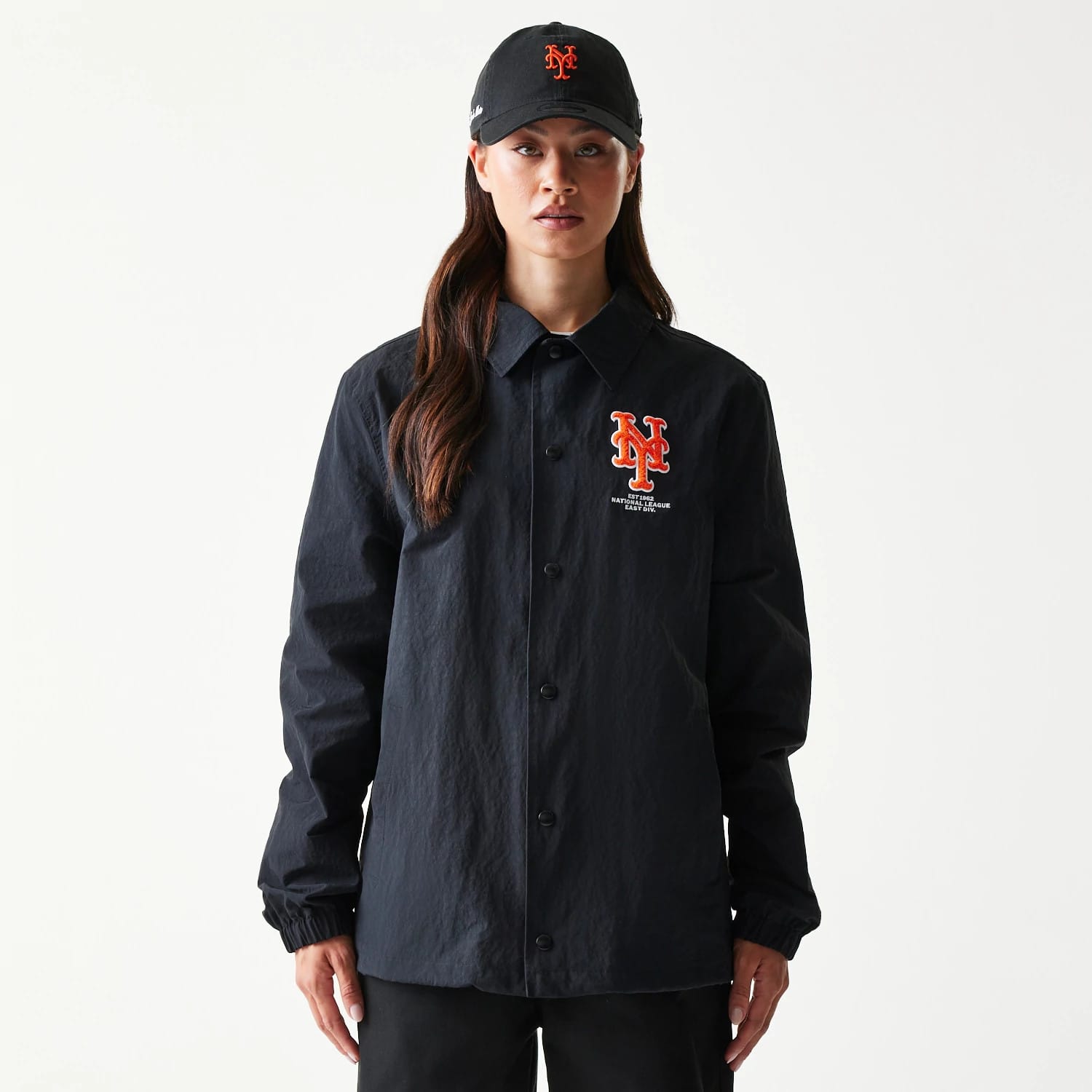 New Era New York Mets MLB Coaches Black Jacket, front view on-model showing the embroidered orange and white New York Mets logo on the left chest, with a button-down closure and elasticated cuffs paired with a black cap featuring the same logo.