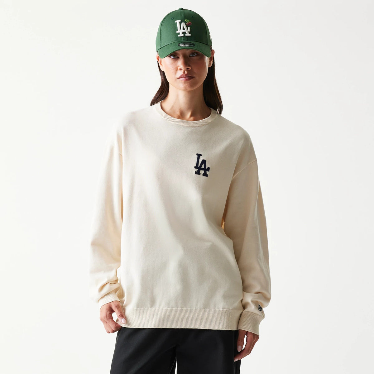 New Era LA Dodgers MLB Essential Open White Knitted Sweater, front view on a model wearing a green cap, showing a black embroidered LA logo on the left chest, with ribbed cuffs and hem on the creamy knitted fabric.