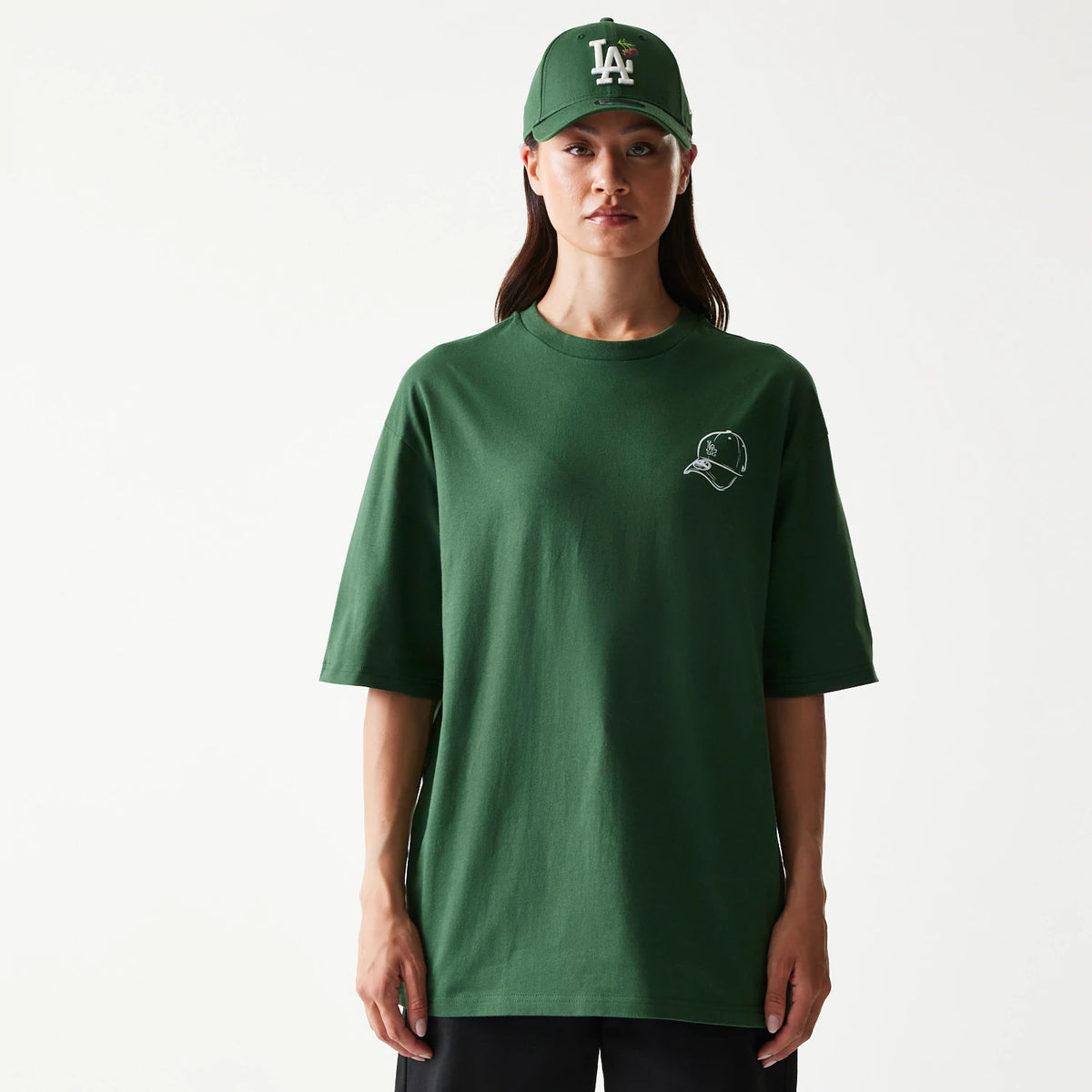 New Era LA Dodgers MLB Baseball Graphic Dark Green Oversized T-Shirt, front view on-model showing a dark green oversized fit with small embroidered cap graphic on the left chest and styled with a matching green cap with an embroidered LA logo.